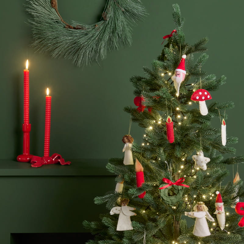 Ein geschmückter Weihnachtsbaum und rote Kerzenhalter stehen dekorativ vor einer dunkelgrünen Wand.