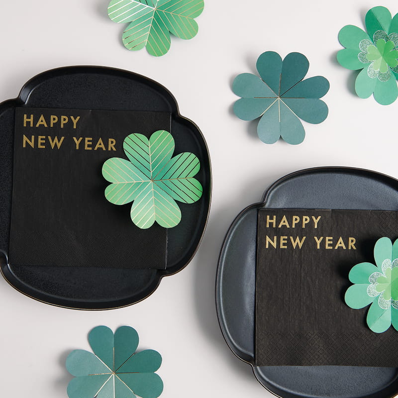 Schwarze Servietten Happy New Year, dekoriert auf Tellern und Glücksklee aus Papier