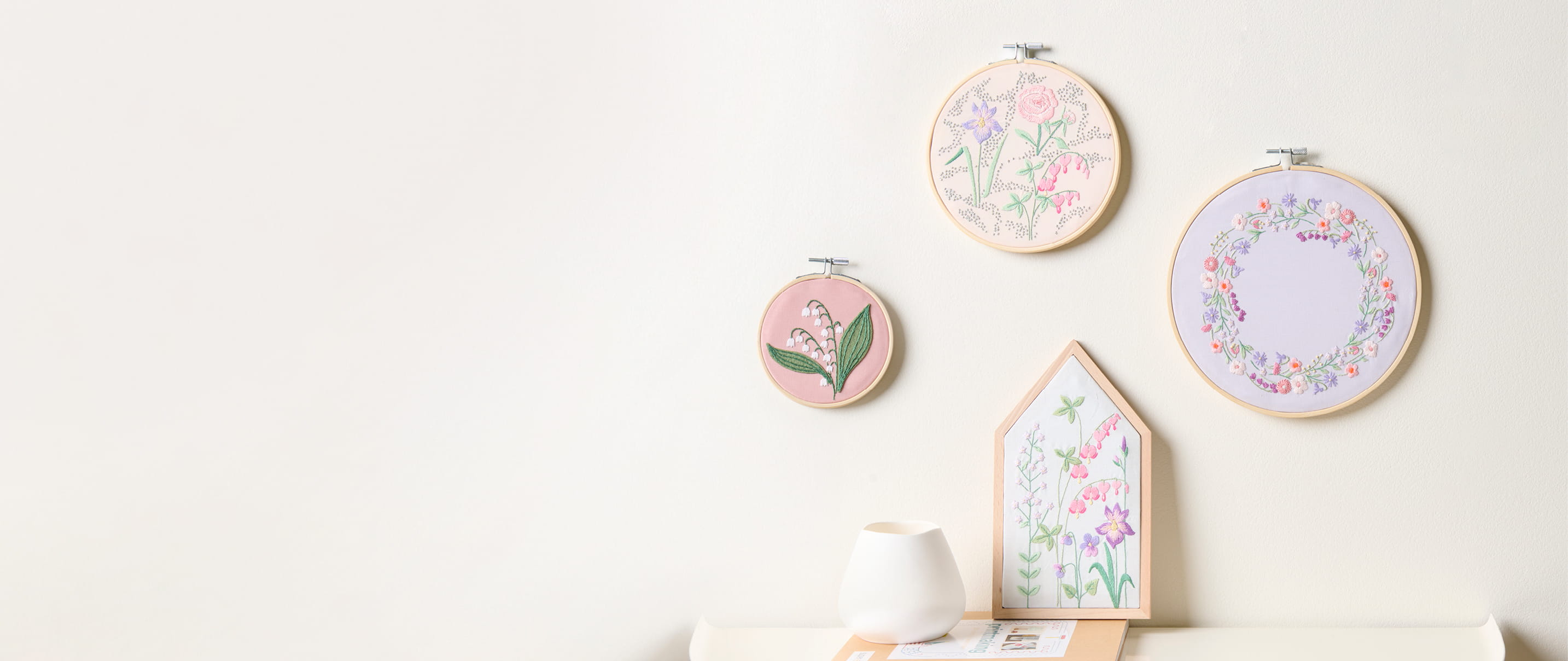 Stickbilder mit floralen Stickdesigns aus der Kollektion The Sky is the Limit hängen an einer Wand.