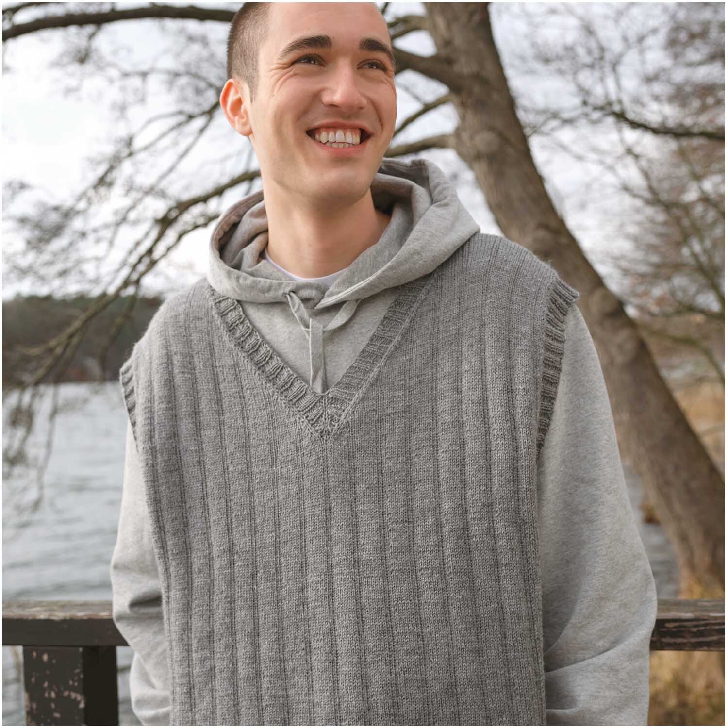 Essentials Fine Fine Merino: Lächelnder Mann in grauem Strickpullunder vor einem See im Hintergrund.