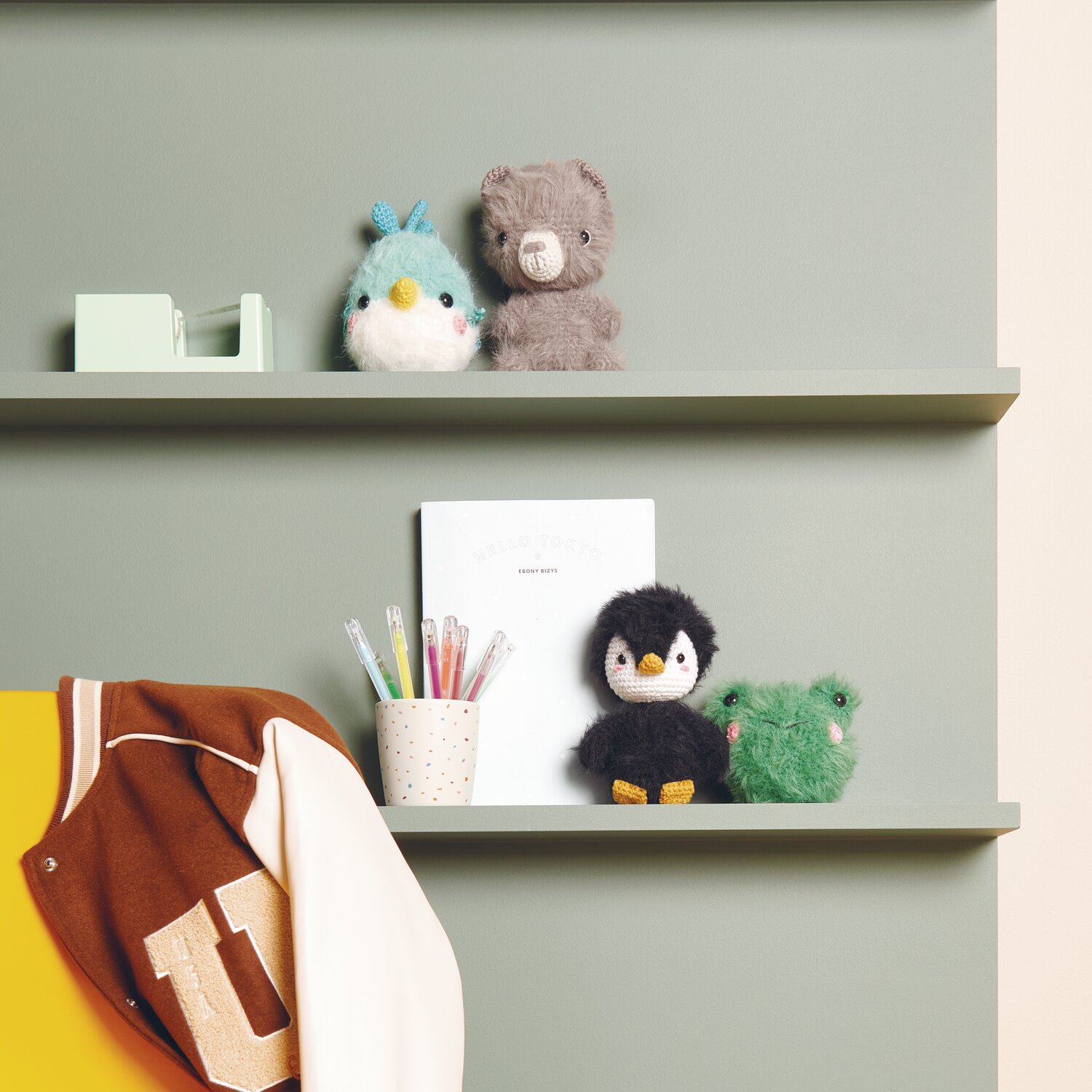 Ricorumi Furry Animals auf einem Regal mit Stiften und Jacke. Farben: Türkis, Schwarz, Grün.