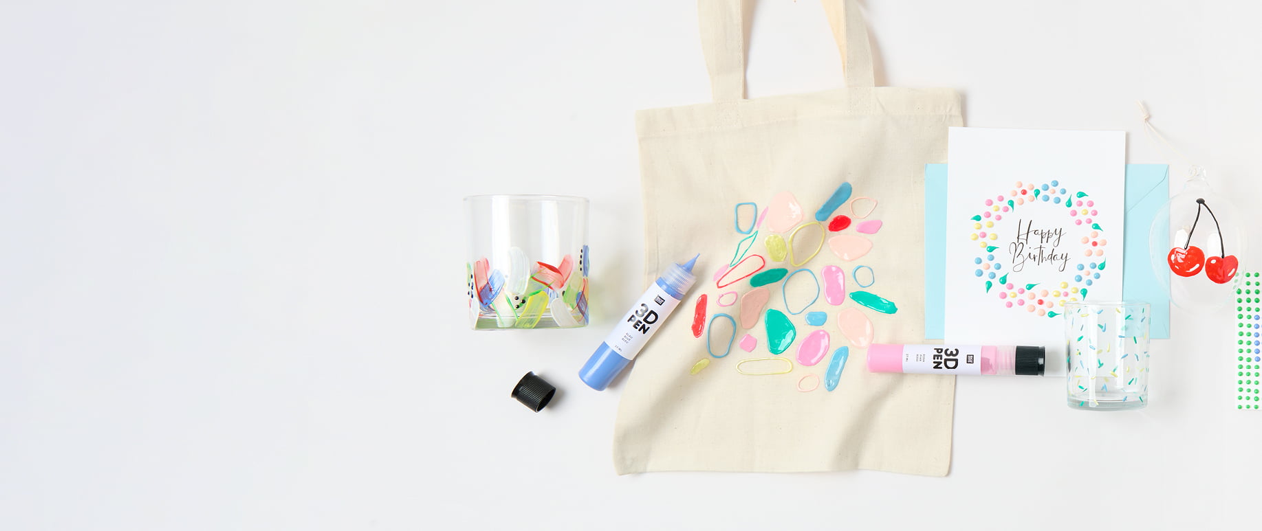 Bunt bemalte Karte, Taschen und Gläser mit 3D- und Perlen-Effekten, liegen umgeben von bunten 3D-Pens auf grauem Hintergrund.