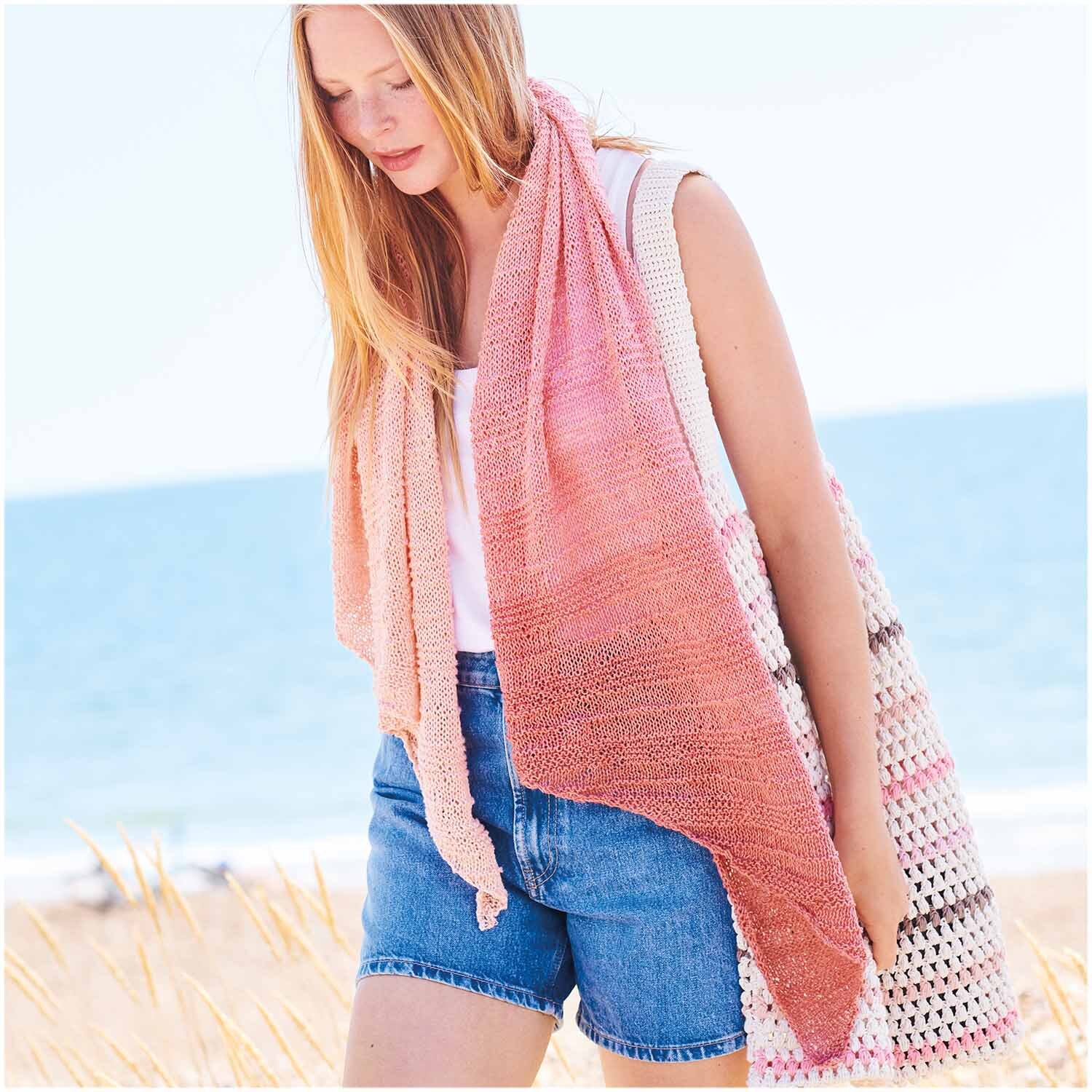 Creative Cotton Dégradé Lucky 8: Frau am Strand mit apricotfarbenem Schal von Rico Design, kombiniert mit Jeansshorts und Tasche.