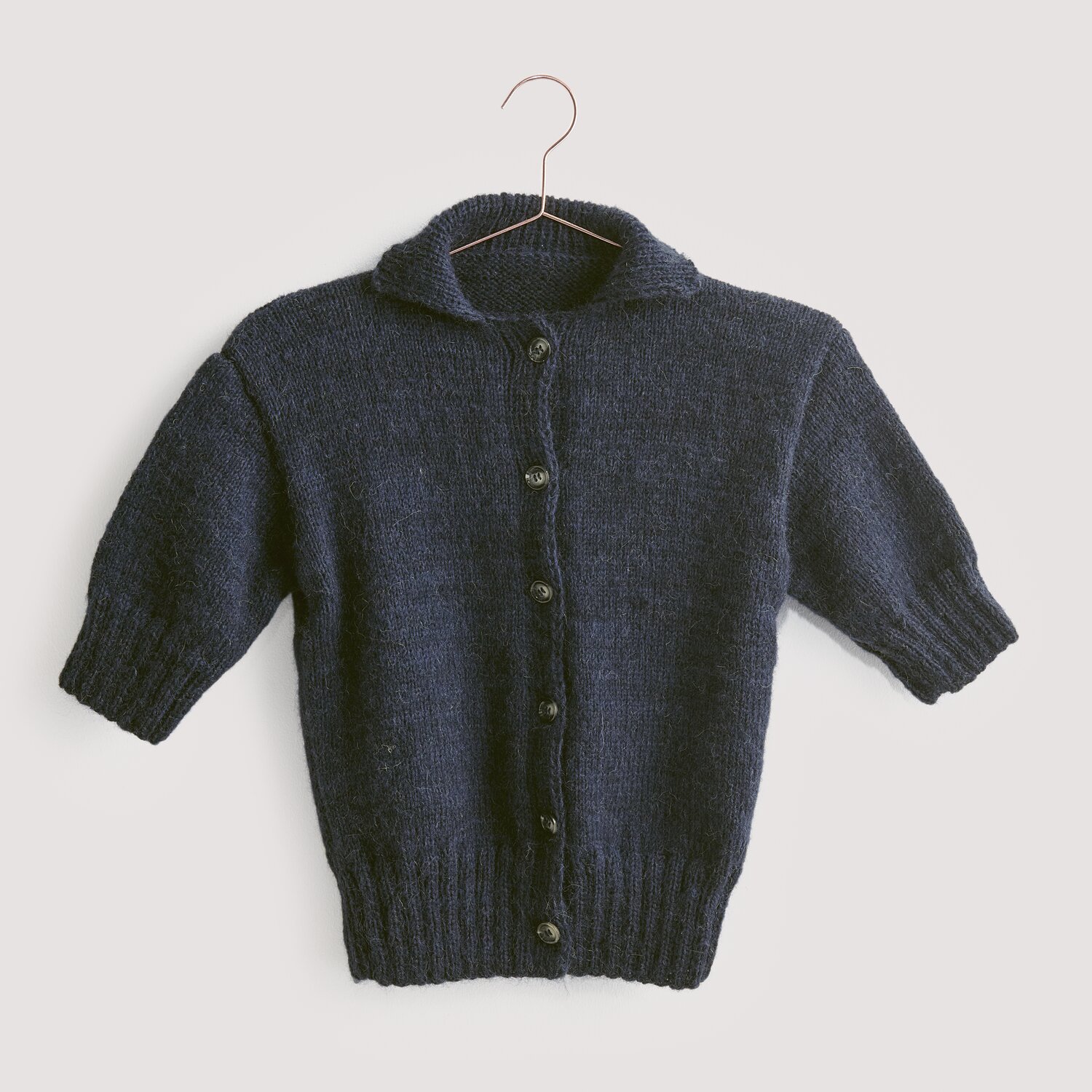 Luxury Knits - Premium Natural Fibres Sprachauswahl deutsch von Rico Design Strickset Jacke Modell 14 aus Luxury Knits: Dunkelblaue Strickjacke aus Premium Natural Fibres, hängend an einem Kleiderbügel.