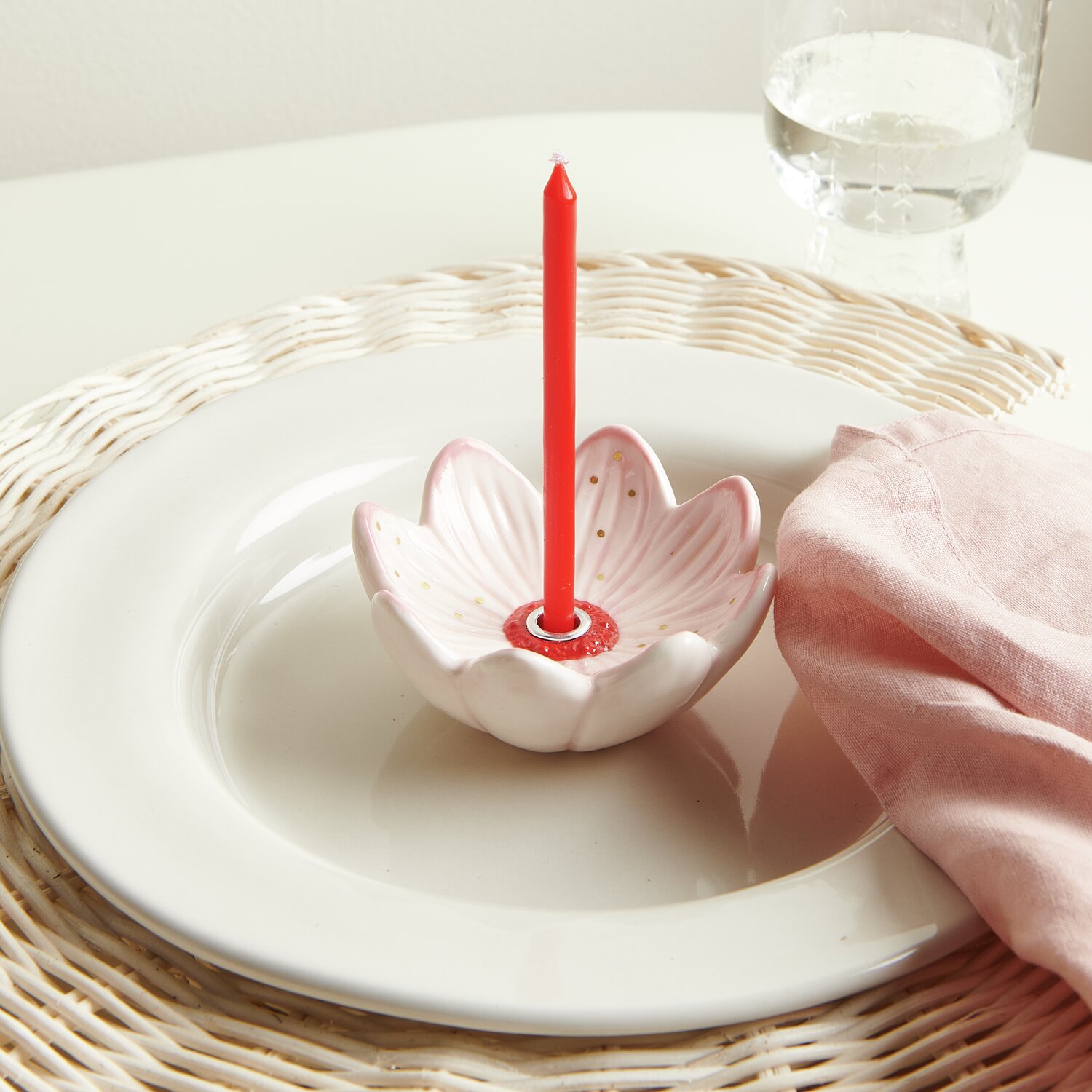 Keramik Kerzenhalter Blüte: Weißer Rattan Deko-Teller mit rosa Kerzenhalter und roter Kerze.