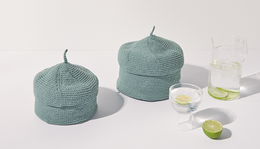 Häkelanleitung Korb mit Deckel aus Essentials Organic Cotton aran: Zwei gehäkelte Körbe in Blaugrün neben einem Glas Wasser und einer Limette.