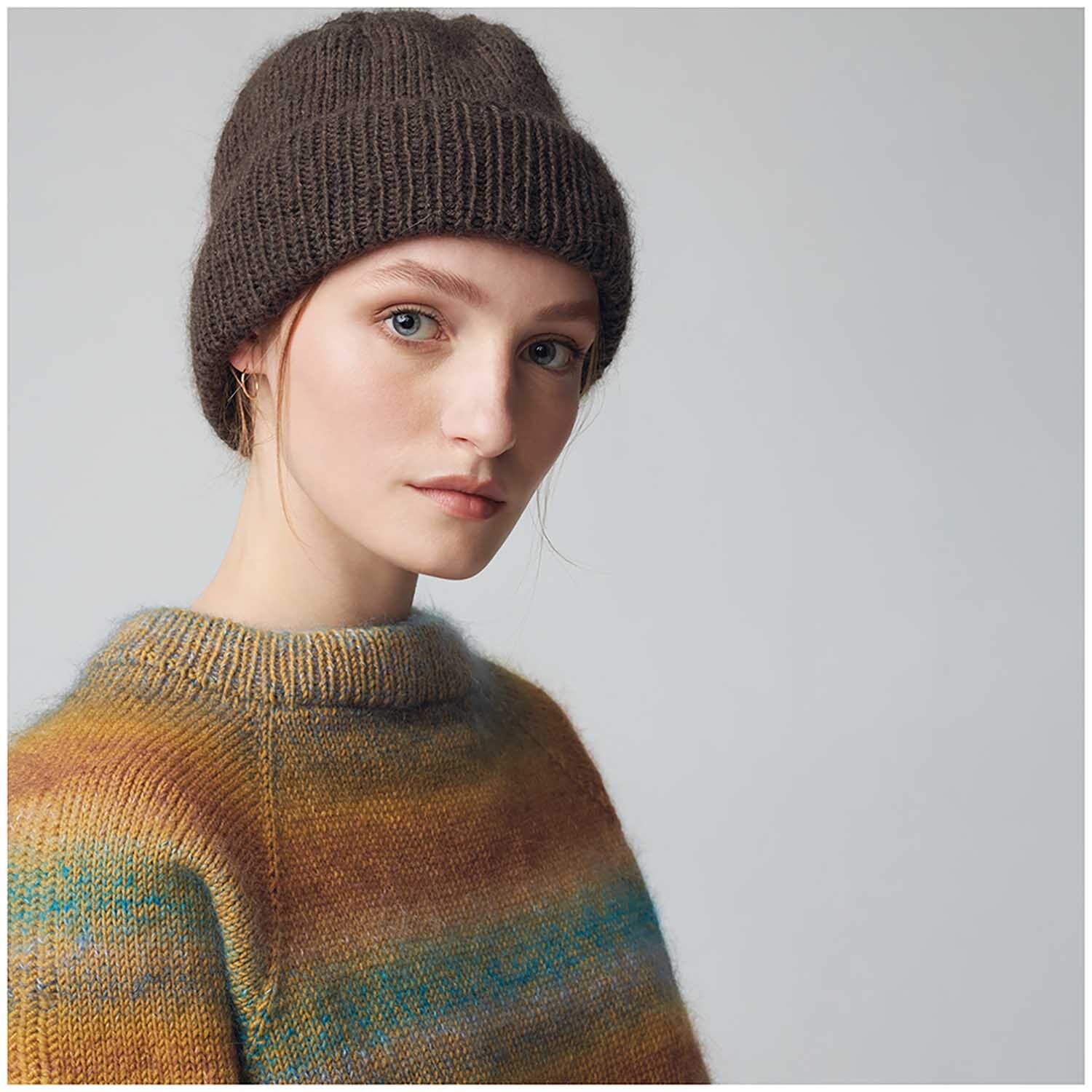 Essentials Merino dk: Frau trägt gestrickte Mütze und Pullover in warmen Erdtönen, ideal für kühle Tage.