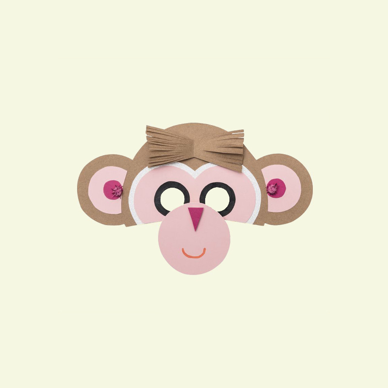 Eine gebastelte Maske in Form eines Affengesichts liegt auf gelben Hintergrund. 