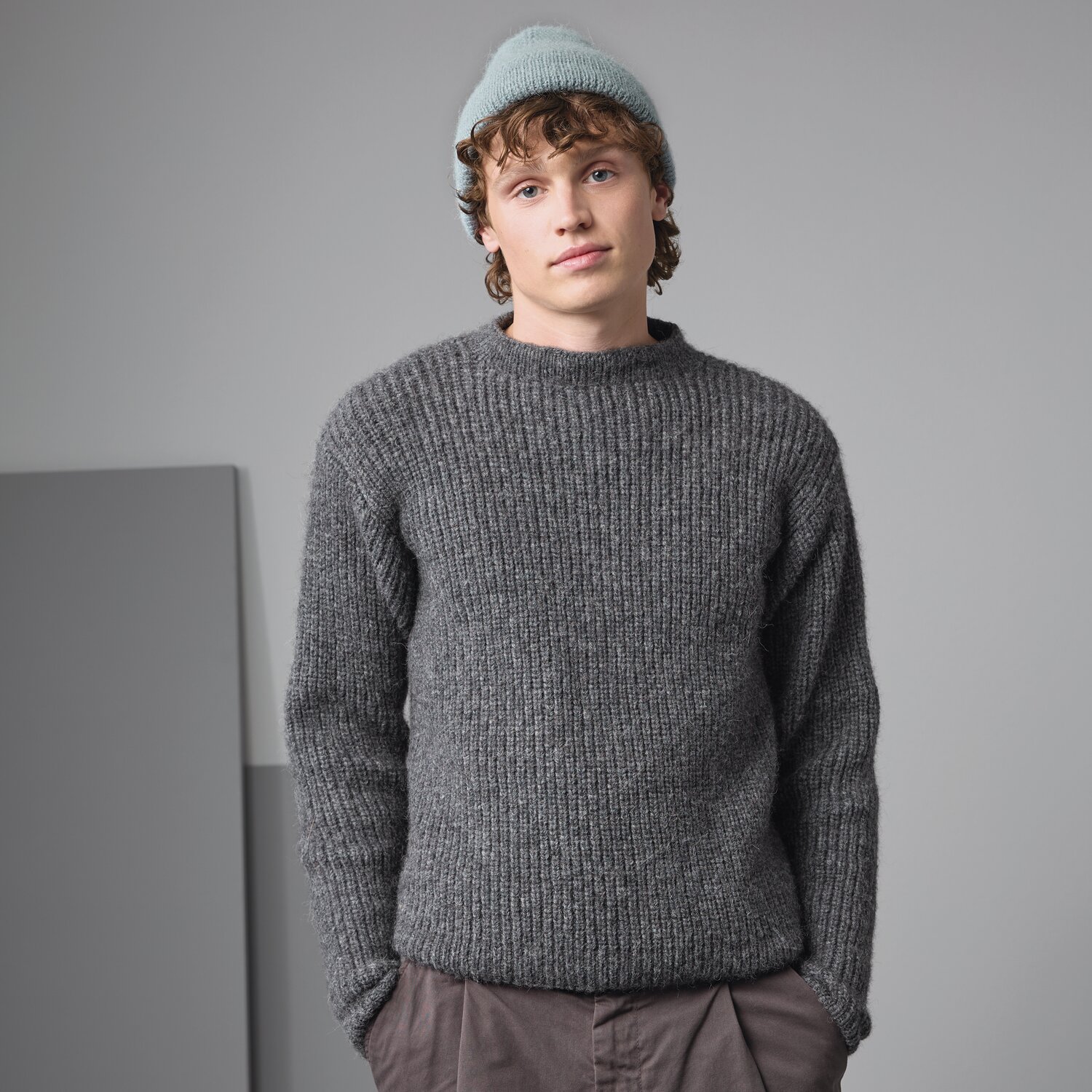 Strickset Pullover Modell 13 aus Made by Me Men No. 3 von Rico Design Strickset Pullover Modell 13: Junger Mann trägt grauen Pullover, kombiniert mit hellblauer Mütze und brauner Hose.