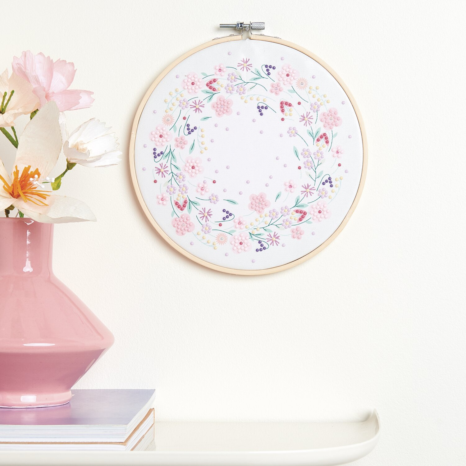 Diamond Painting DIY-Set Funkelnder Blumenkranz, Ø20cm, zeigt florales Design in zarten Pastelltönen an einer weißen Wand.