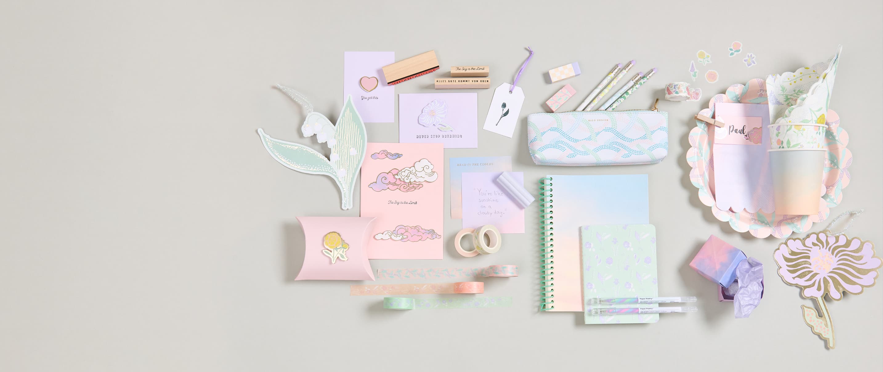 Papeterie-, Party und Geschenkprodukte mit Himmel- und Blumendesigns liegen angeordnet auf grauem Hintergrund.