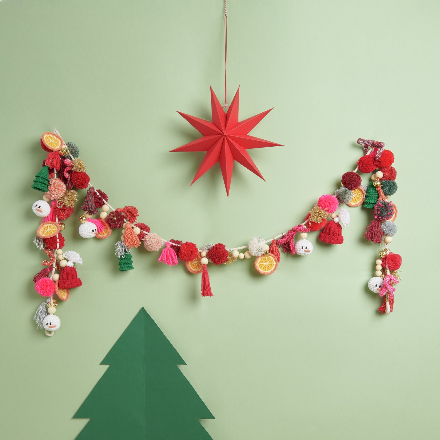 Ricorumi DIY Adventskalender von Rico Design Ricorumi DIY Adventskalender: Bunte Girlande mit Pompons und Anhängern vor grünem Hintergrund.