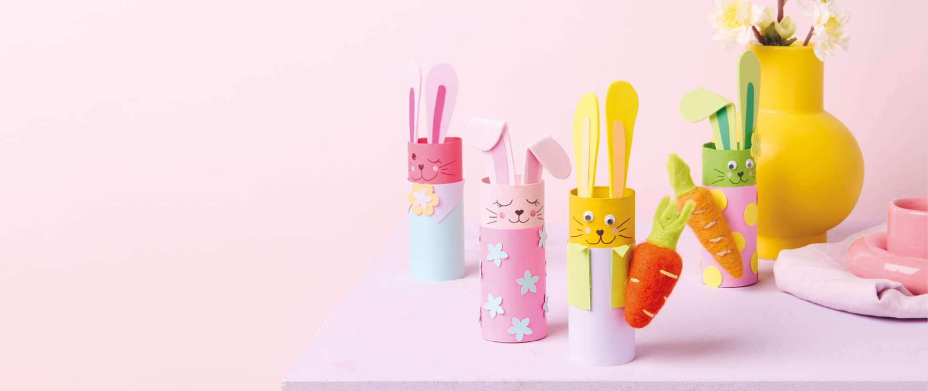 Bunte Hasenfiguren aus Papierrollen stehen vor einem rosa Hintergrund.