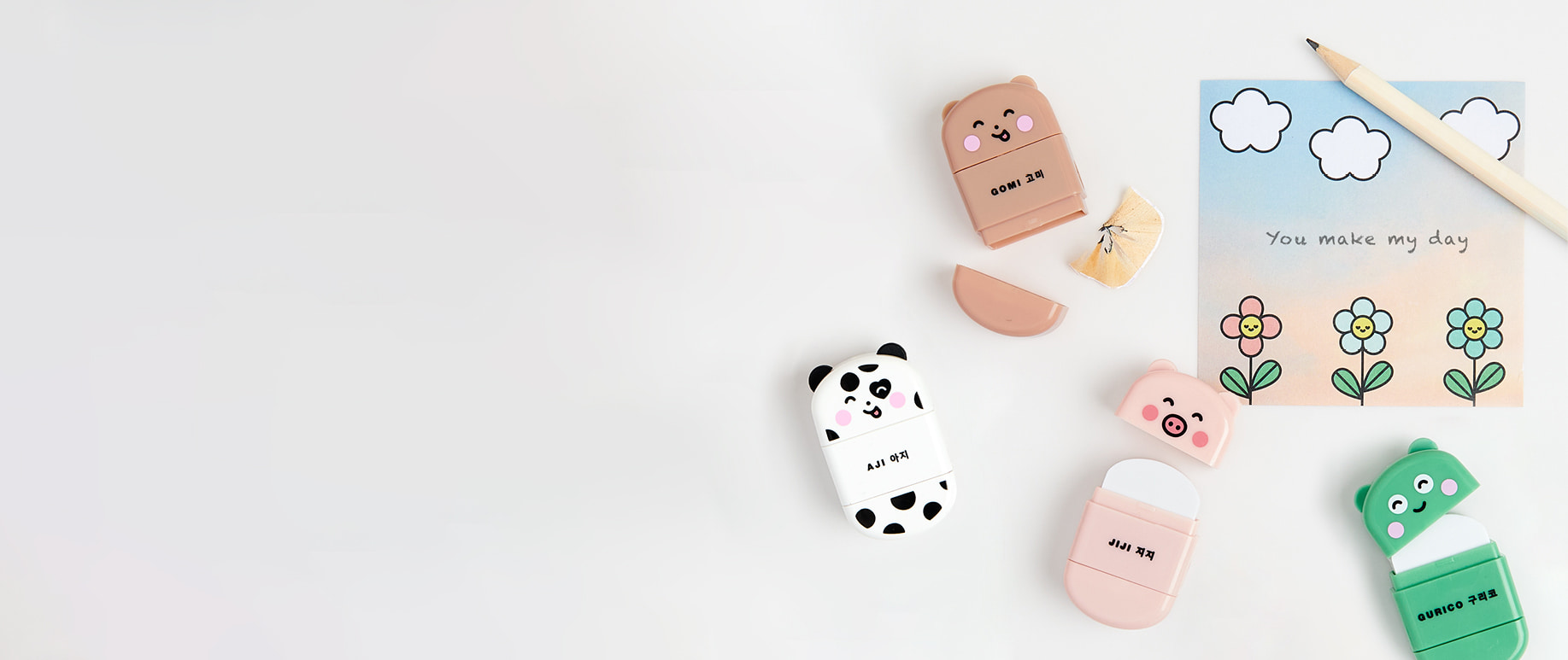 Radiergummis in Tierformen mit Anspitzer liegen umgeben von Stift und Notizzettel auf grauem Hintergrund.