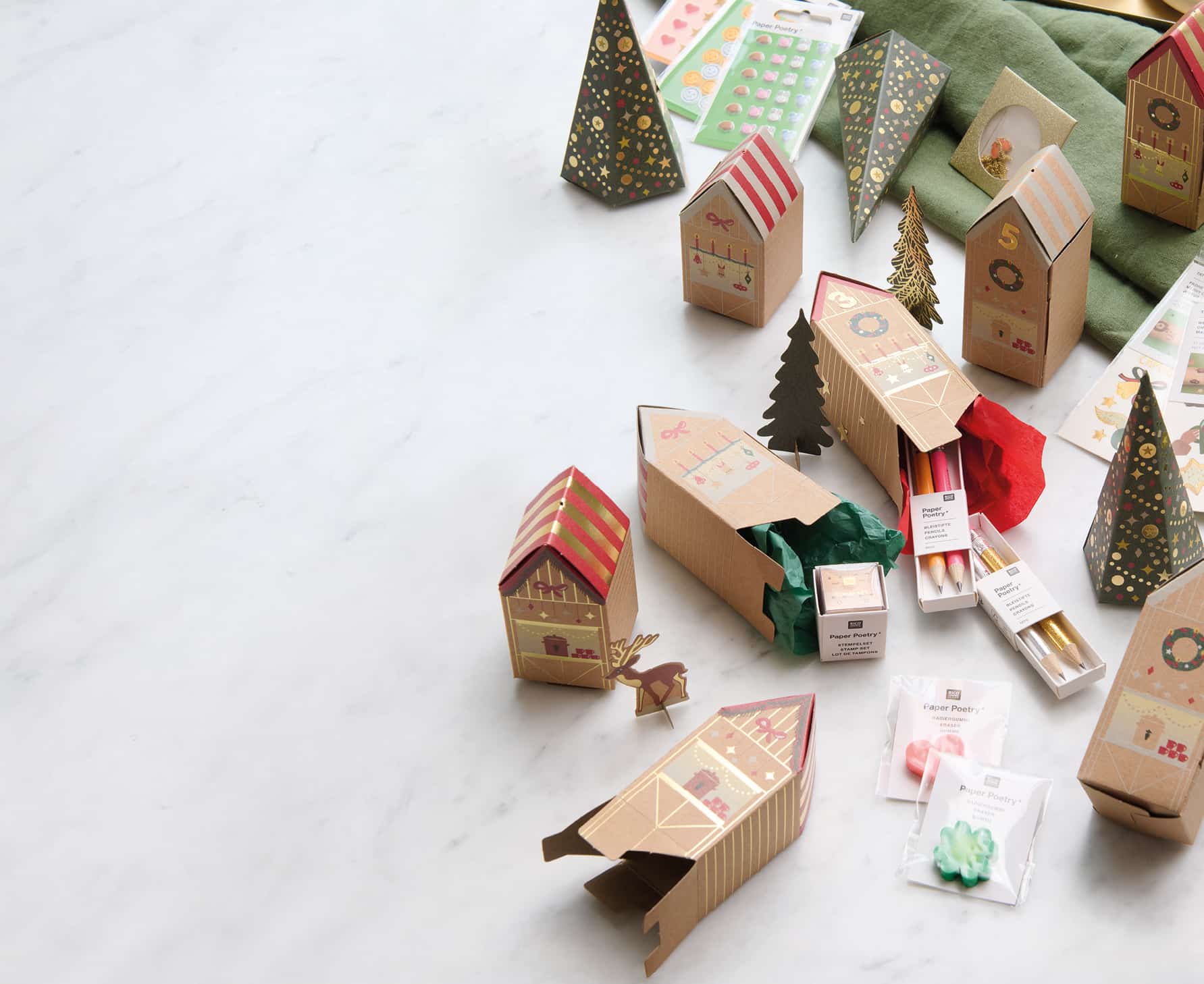 Adventskalender Häuser liegen ausgebreitet auf einem Tisch und werden mit kleinen Geschenken befüllt.