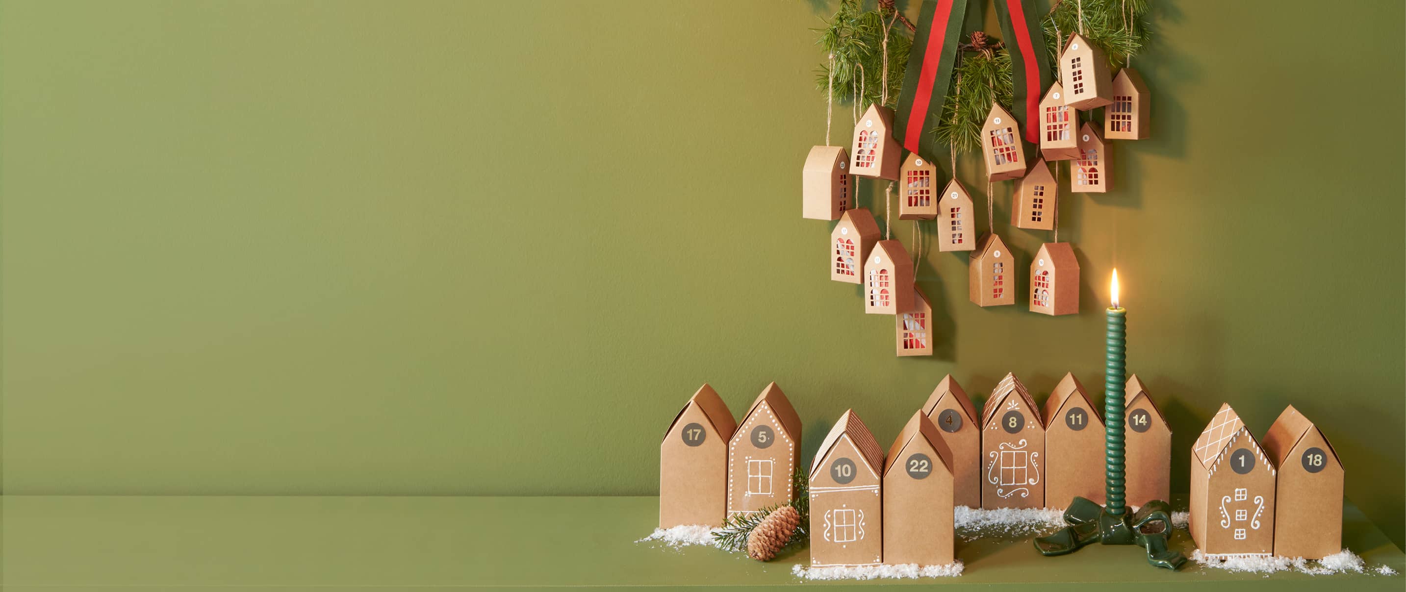 Adventskalender in Form von Papphäusern sind weihnachtlich aufgestellt und an einem Kranz dekoriert