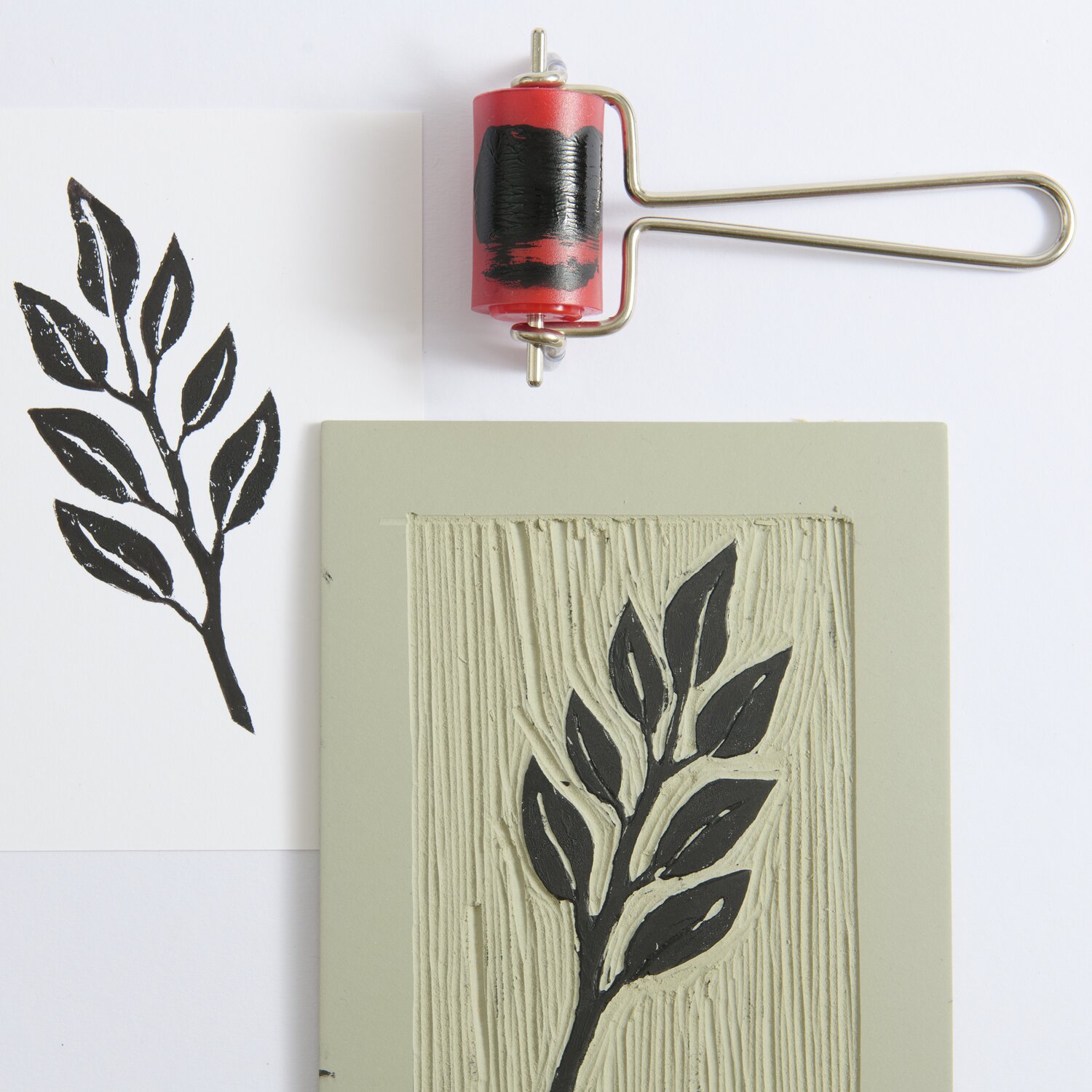 Linolwalze von Rico Design, Ø3cm, in Rot und Schwarz, neben einem Blattmotiv auf Linoleumplatte.