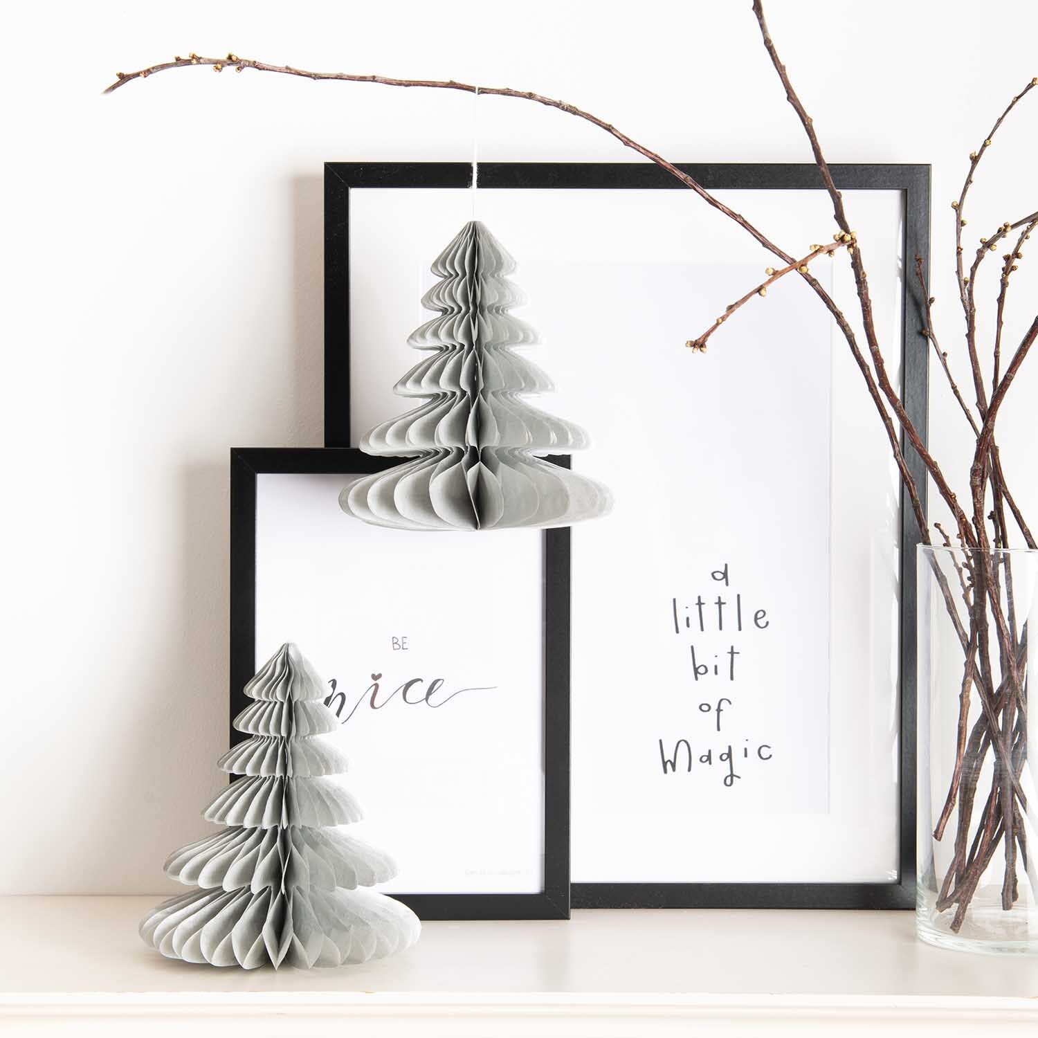 Wabenpapier Tannenbäume 20cm 2 Stück Farbe Silber von Rico Design Wabenpapier Tannenbäume 20cm 2 Stück in Silber vor gerahmten Bildern und Zweigen.