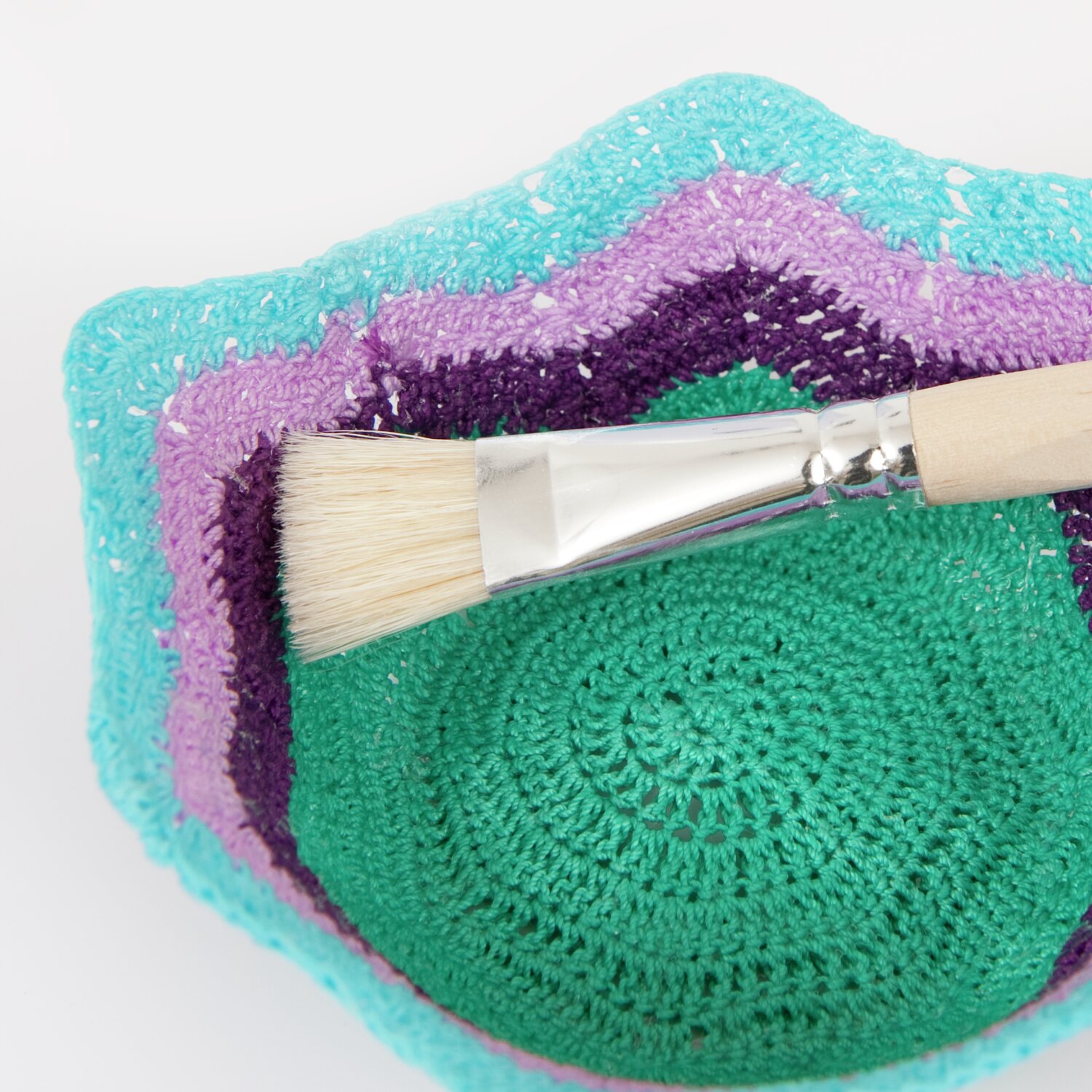 Textilsteif 105g von Rico Design Textilsteif, Pinsel auf gehäkeltem Untergrund in Türkis, Lila und Grün, ideal für kreative Projekte.