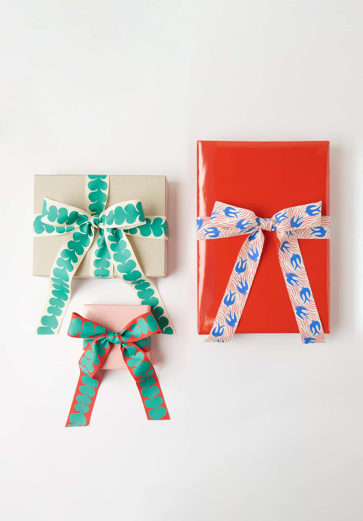 Drei Geschenke mit bunten Schleifen auf weißem Hintergrund: ein rotes, ein beiges und ein kleines rosa Geschenk