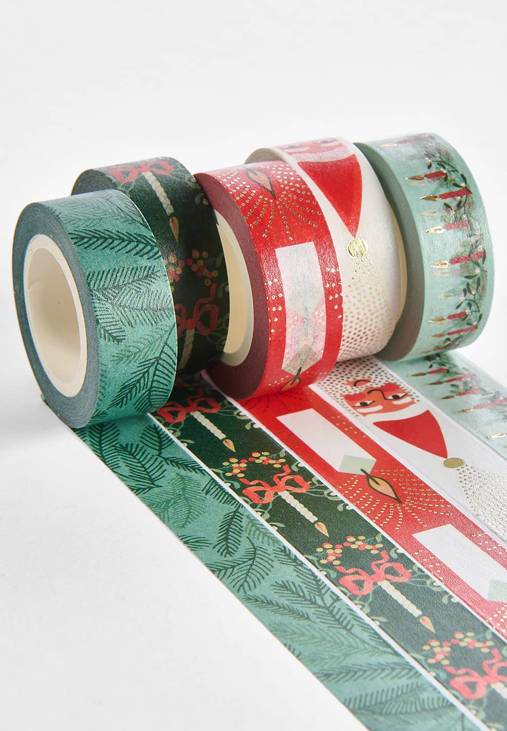 Washi Tape Rollen mit weihnachtlichen Motiven liegen ausgerollt und aneinandergereiht auf einem hellgrauen Untergrund.