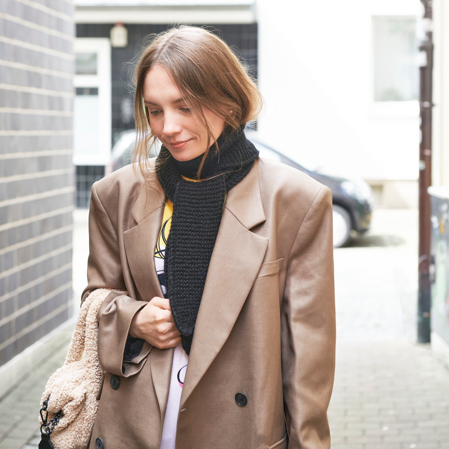 Strickset Mini Schal Modell 03a: Frau trägt schwarzen Schal, braunen Mantel, steht draußen.