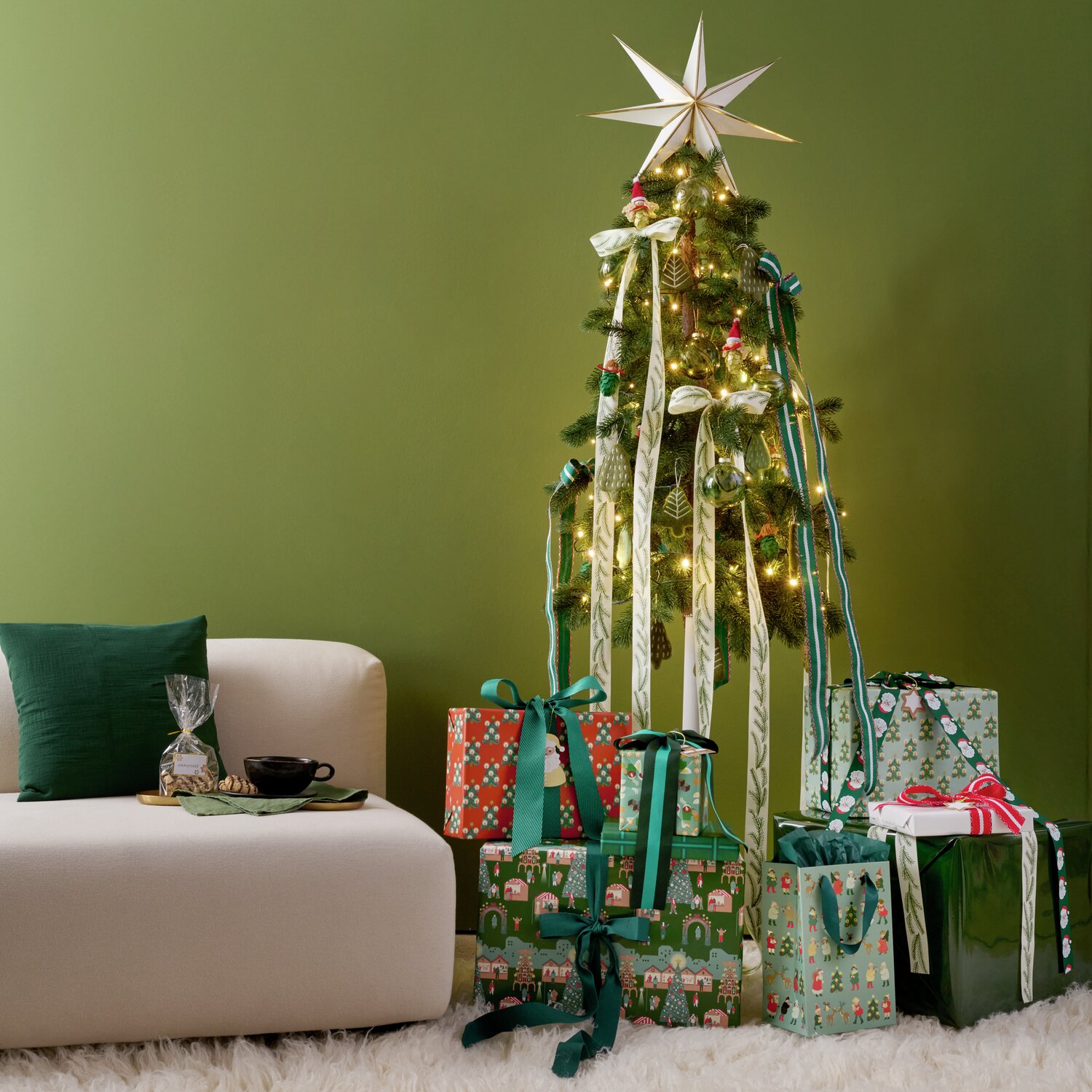 Auf dem Bild ist ein stilvoll dekorierter Weihnachtsbaum von Rico Design zu sehen, geschmückt mit handgefilzten Tannenaufhängern in Khaki. Der Baum ist umgeben von festlich verpackten Geschenken.