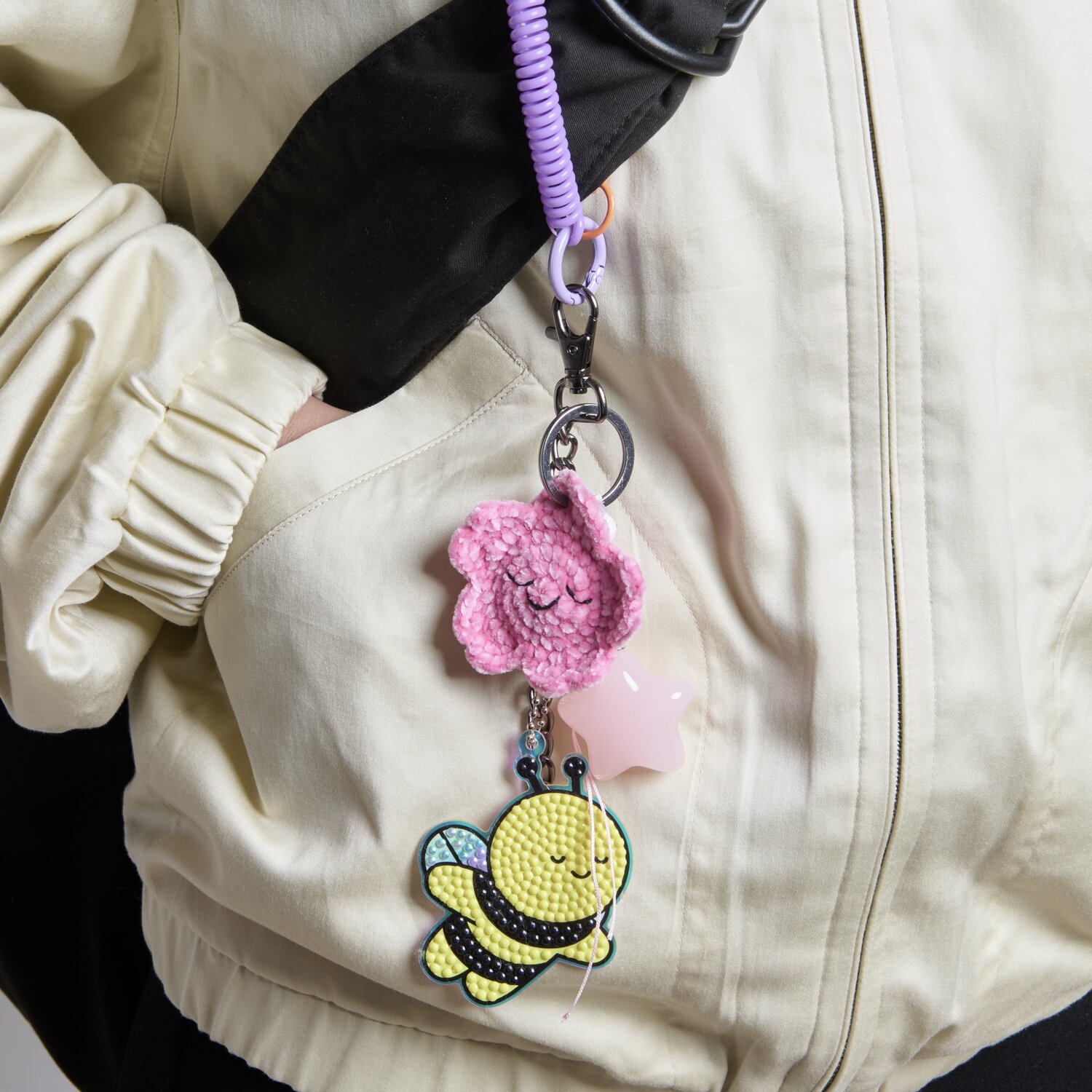 Karabiner mit Kette und Schlüsselring 13cm von Rico Design Karabiner mit Kette und Schlüsselring 13cm, verziert mit rosa Blume und gelber Biene, an einer hellen Jacke befestigt.