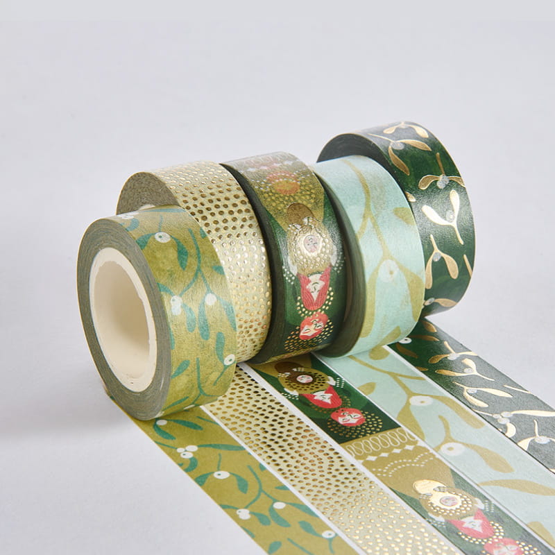 Washi Tape Rollen mit weihnachtlichen Motiven liegen ausgerollt auf grauem Hintergrund.