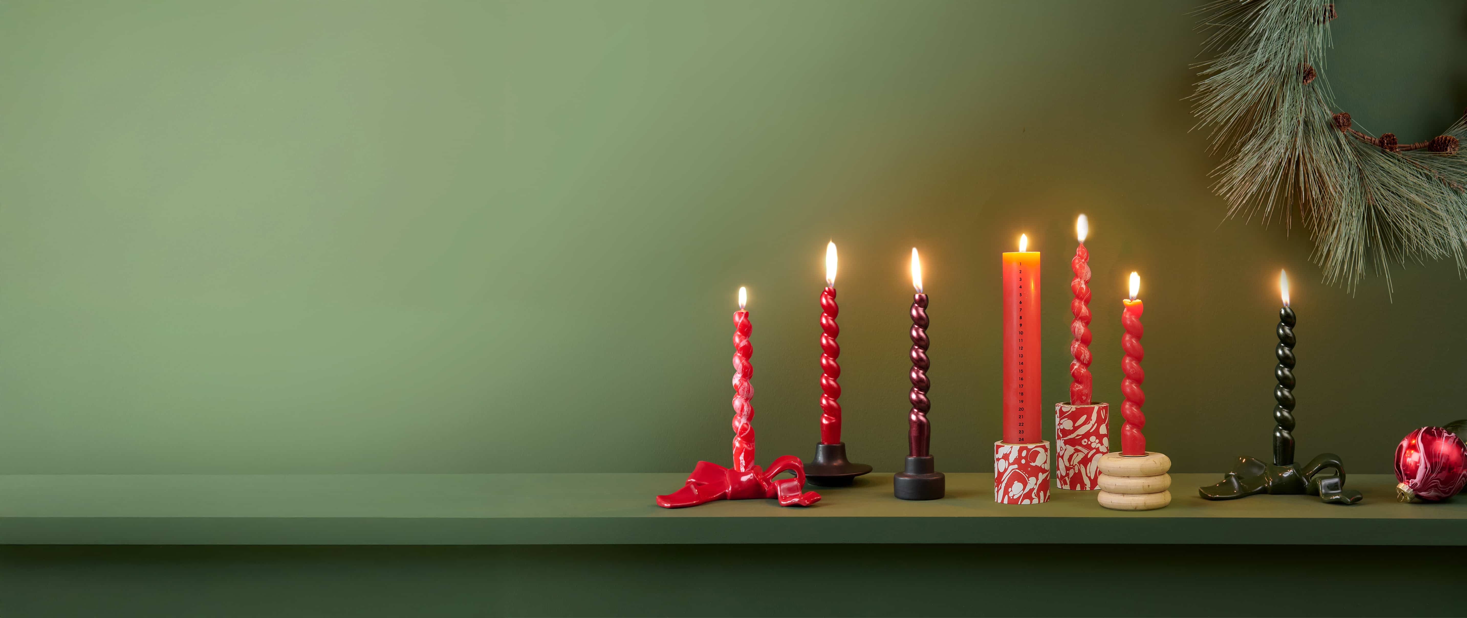 Kerzen und Kerzenhalter in Rot- und Grüntönen sind vor einer grünen Wand dekoriert.