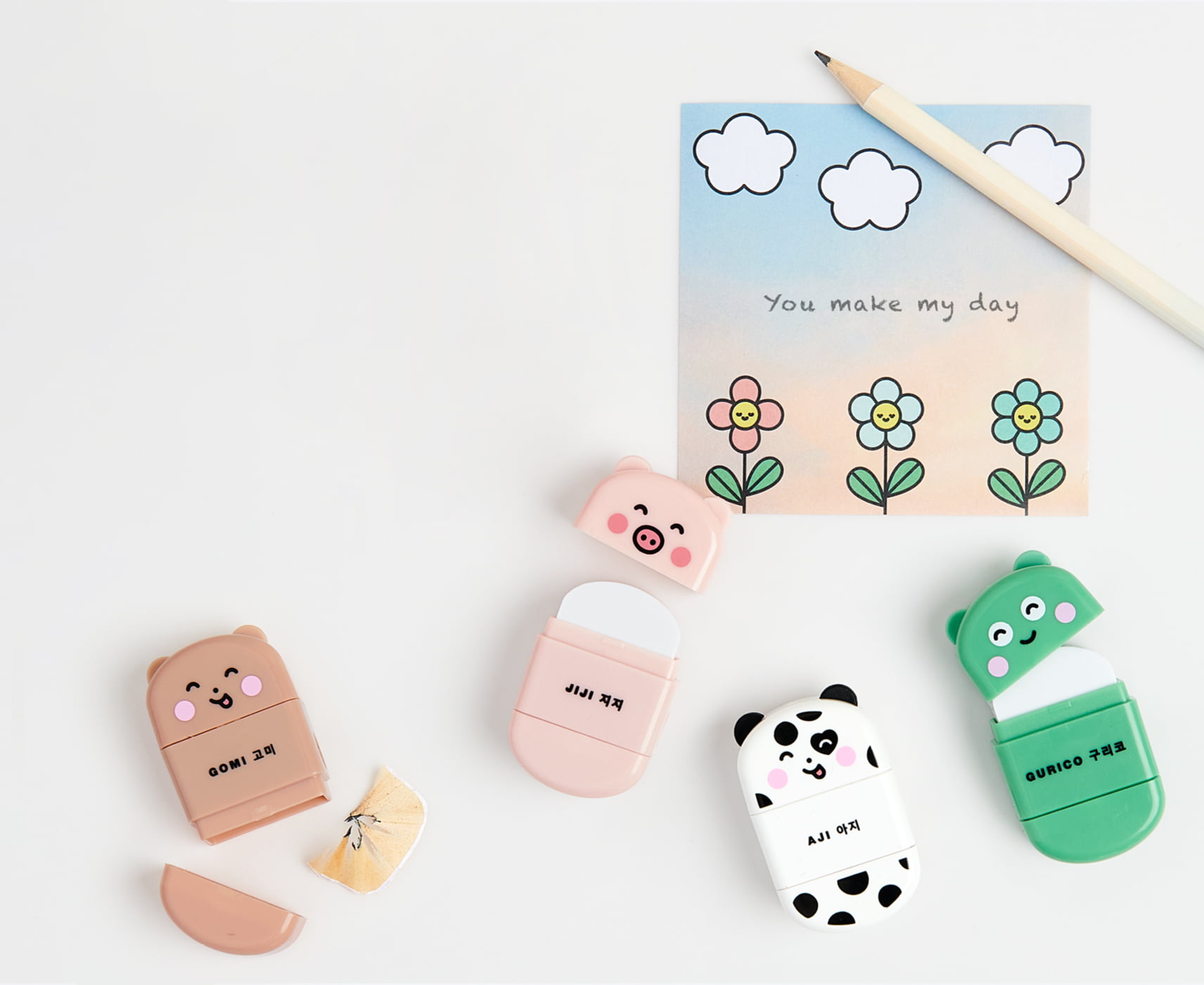 Radiergummis in Tierformen mit Anspitzer liegen umgeben von Stift und Notizzettel auf grauem Hintergrund.