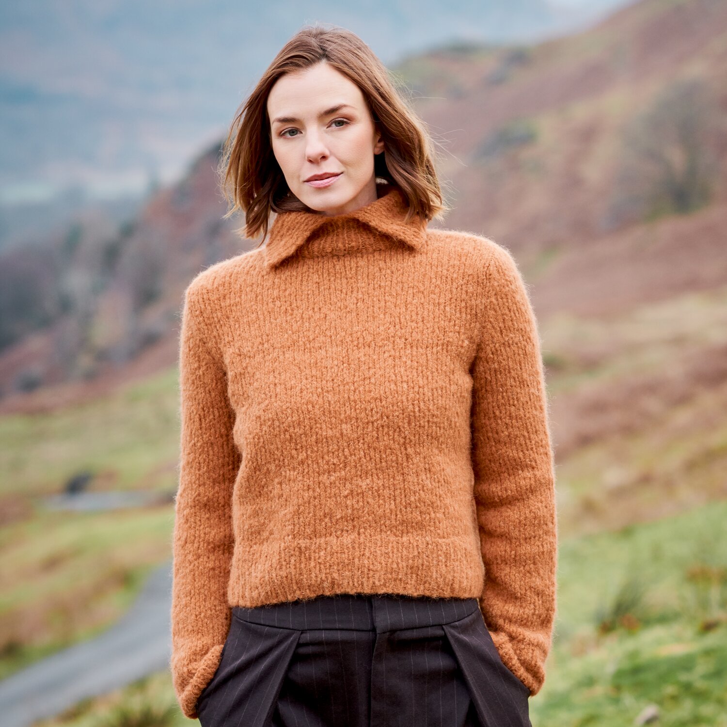 Strickset Pullover Modell 37 aus Lovewool No. 23, locker geschnitten mit breitem Kragen, von Frau getragen, stehend in herbstlicher Hügellandschaft