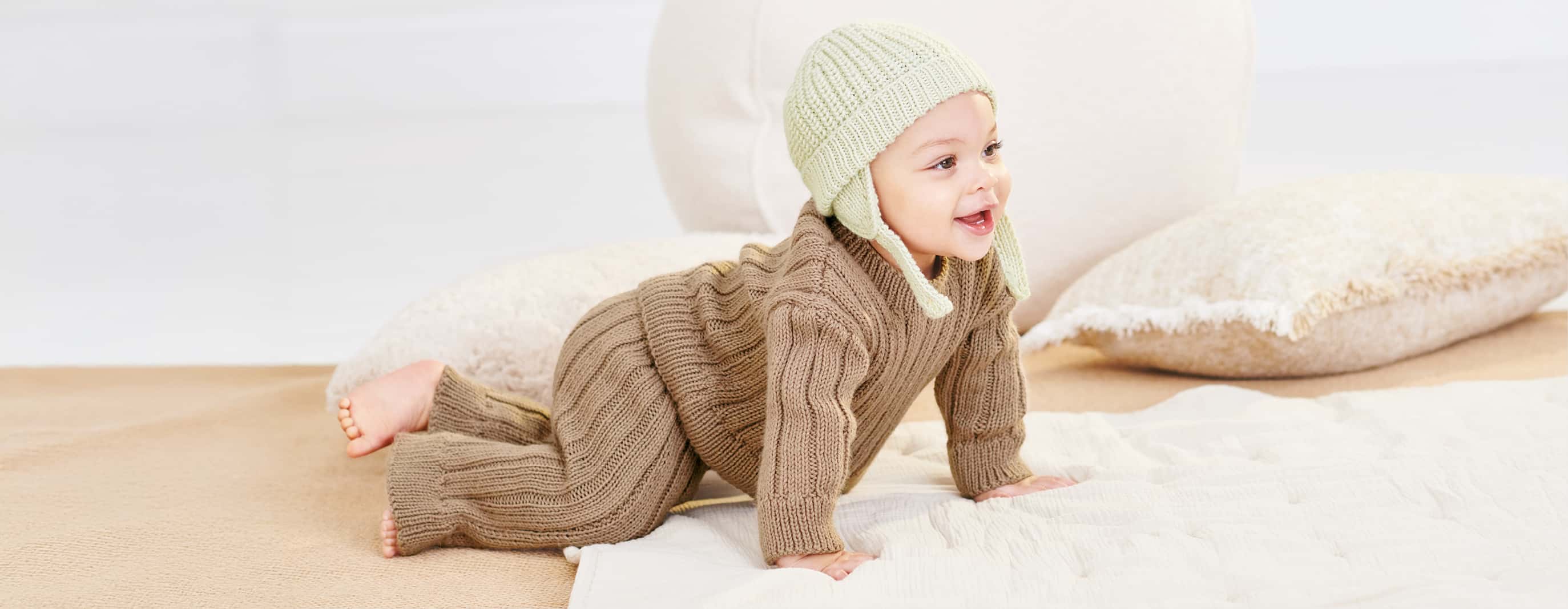 Kleinkind mit gestricktem Outfit und Mütze krabbelt über eine Decke