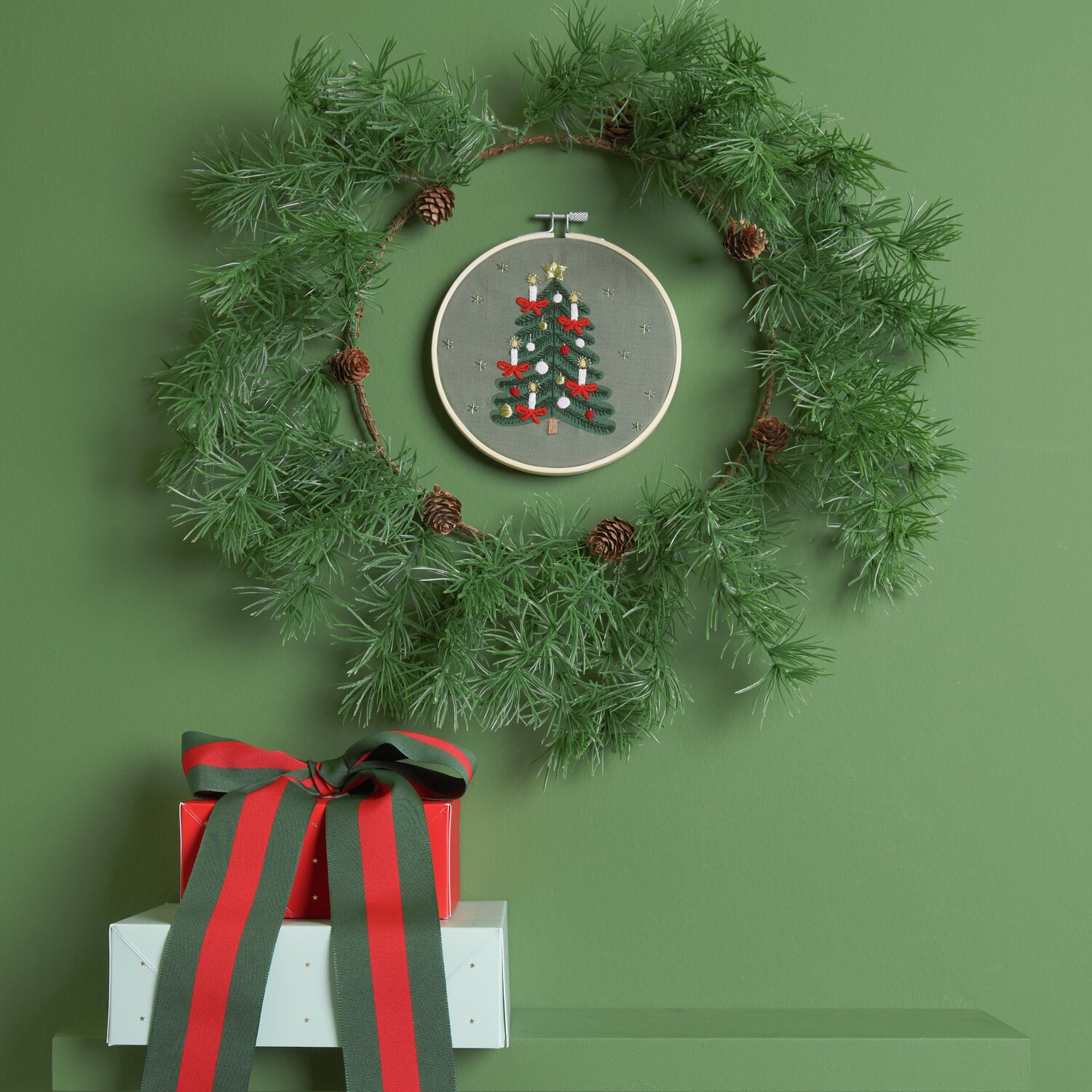 Stickpackung Weihnachtsbaum vorgezeichnet Ø15cm von Rico Design Stickpackung Weihnachtsbaum vorgezeichnet: Ein grüner Kranz mit Stickrahmen und Weihnachtsbaum-Motiv, dekoriert mit Geschenken.