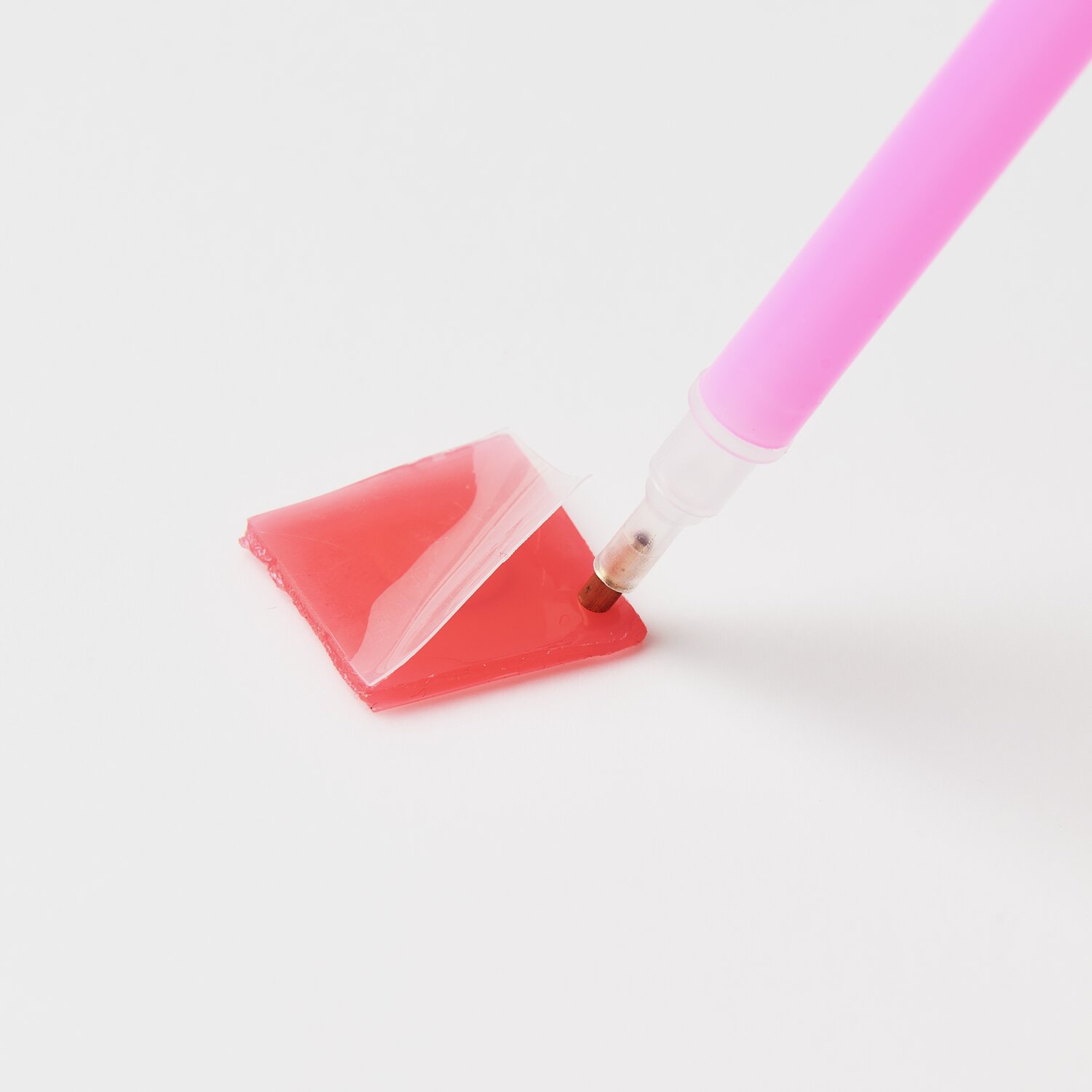 Diamond Painting Masken Tiere, 52-teilig: Ein pinker Stift nimmt rote Klebepaste auf weißem Hintergrund auf.