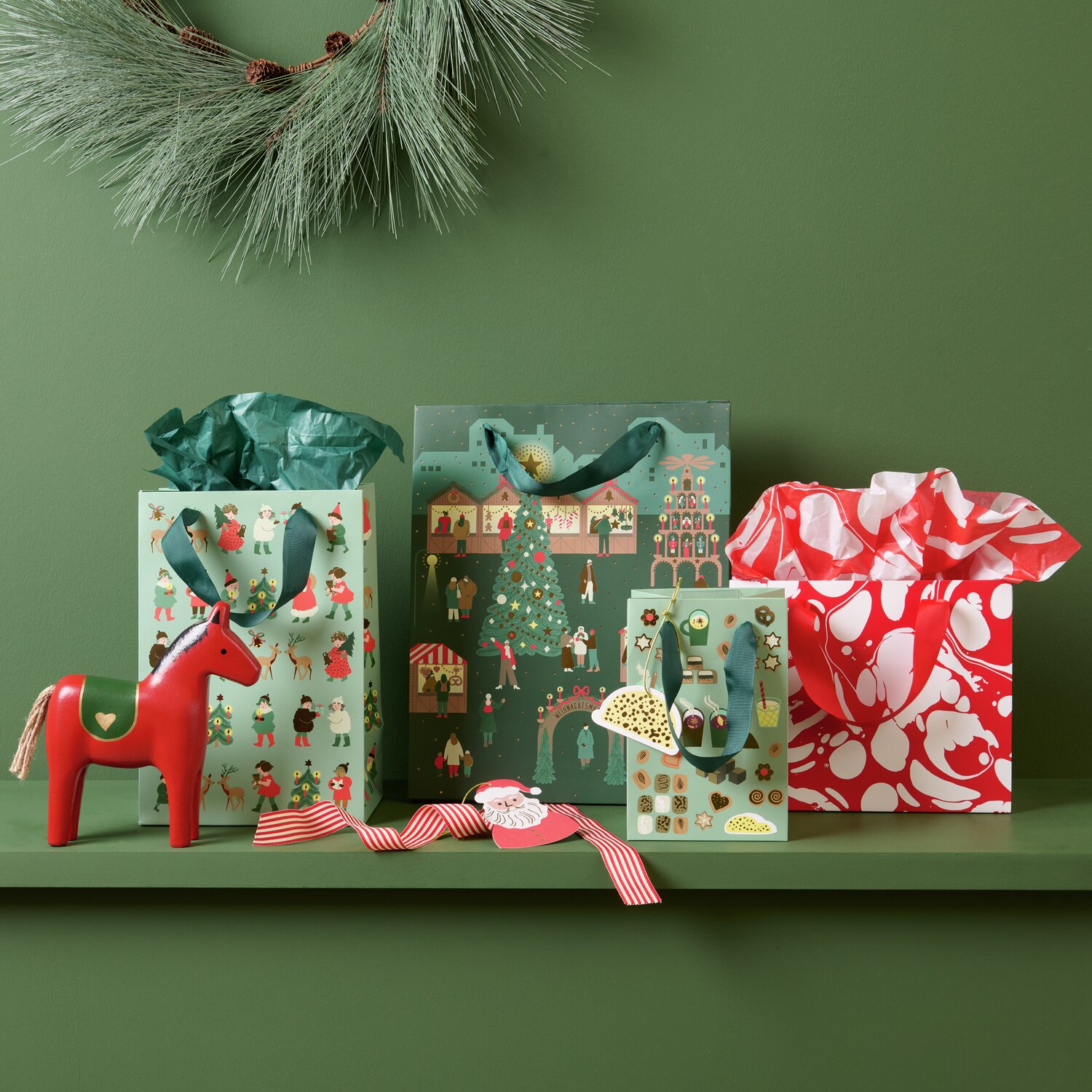 Holzpferd 18,5x4,2x17cm Farbe Rot von Rico Design Geschenktüte Marmor Rot/Weiß S auf grünem Hintergrund mit Weihnachtsmotiven und Holzpferd.