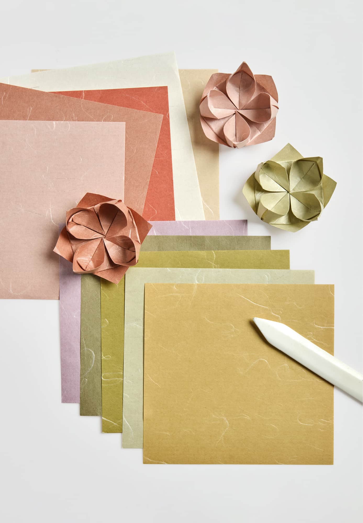Origamipapier und gefaltete Blumen liegen auf grauem Hintergrund.