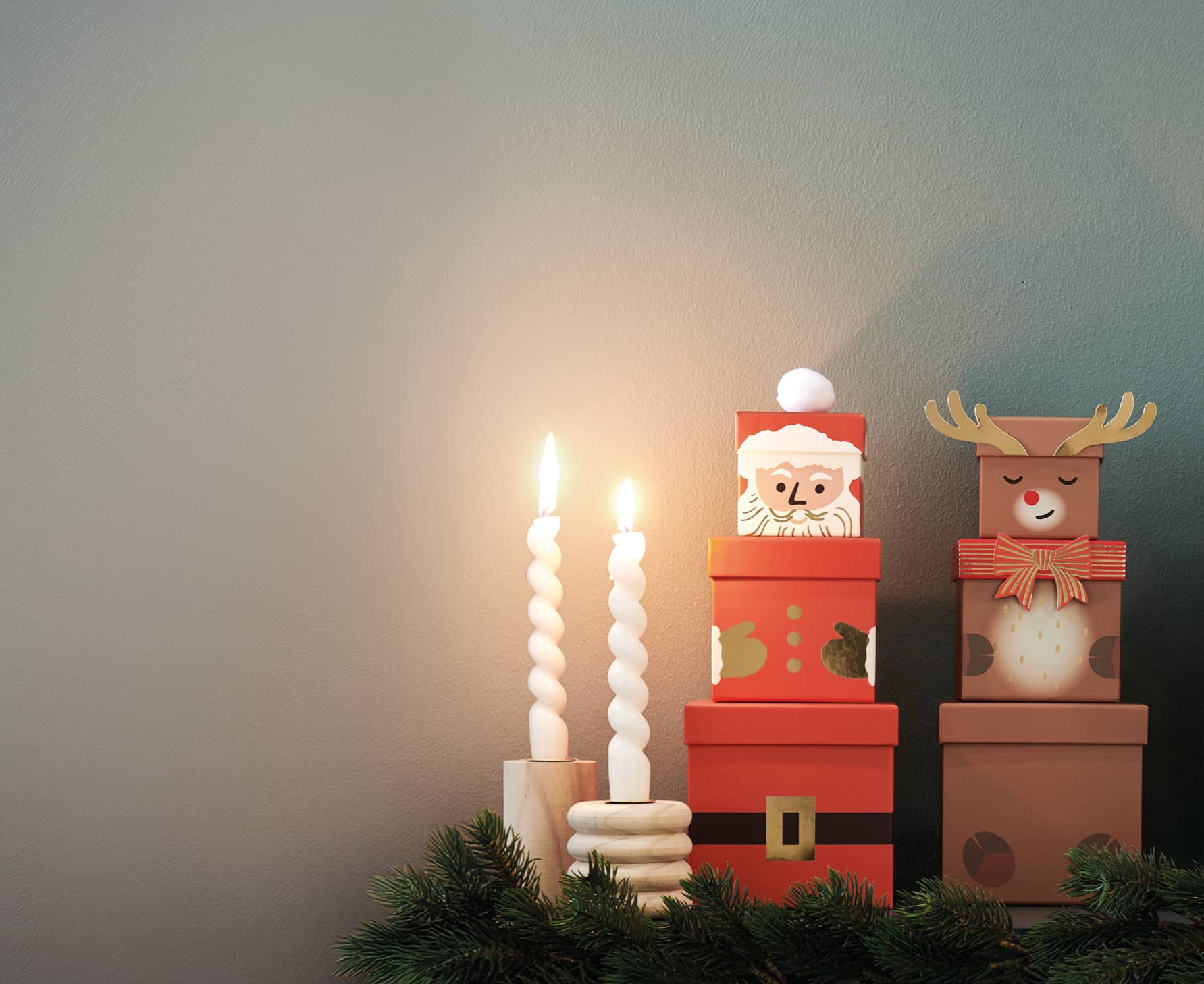 Die Geschenkboxen-Sets mit Weihnachtsmann und Rentier sind weihnachtlich mit Tannenzweigen und Kerzen dekoriert.