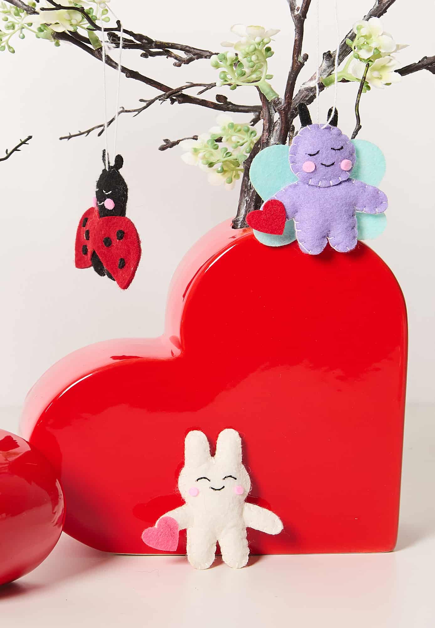 Filzanhänger in Form von Tieren sind dekorativ an Zweigen in einer Vase aufgestellt.