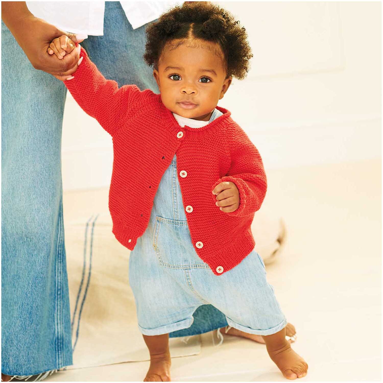 Baby Organic Cotton: Ein Kleinkind trägt einen roten Strickpullover von Rico Design und hält die Hand eines Erwachsenen.