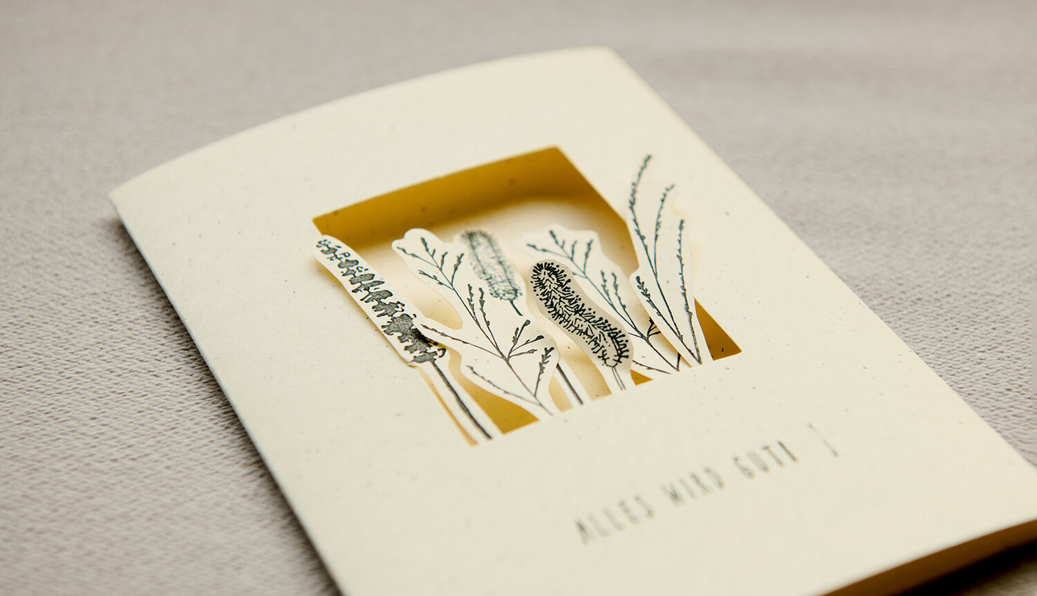 Bastelanleitung in the Meadow Passepartout-Karte mit ausgeschnittenem Fenster, feinen Wiesenblumen-Illustrationen und gelbem Hintergrund, liegend auf hellem Stoff