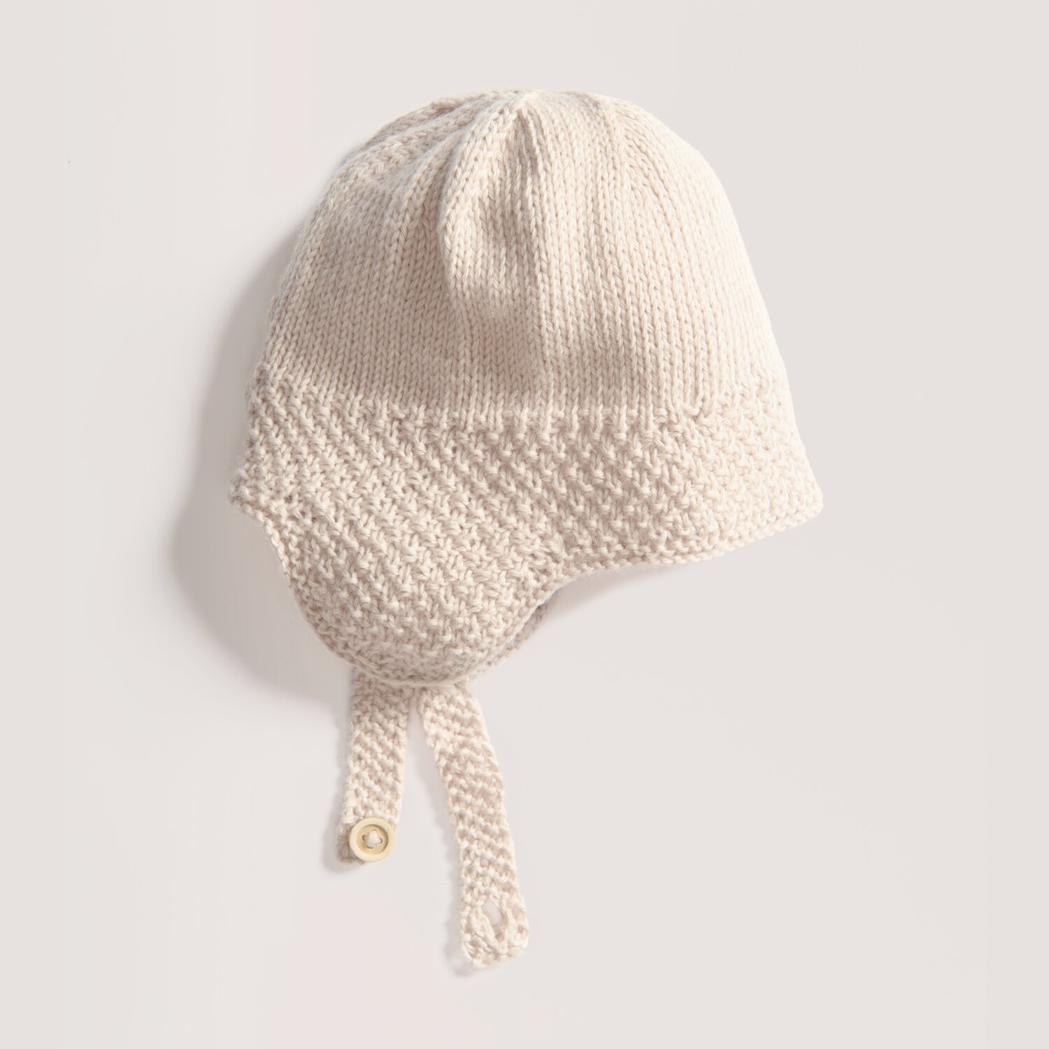 Rico Baby 043: Weiche, naturfarbene Babymütze aus Bio-Baumwolle und Kaschmir mit Knopfverschluss.