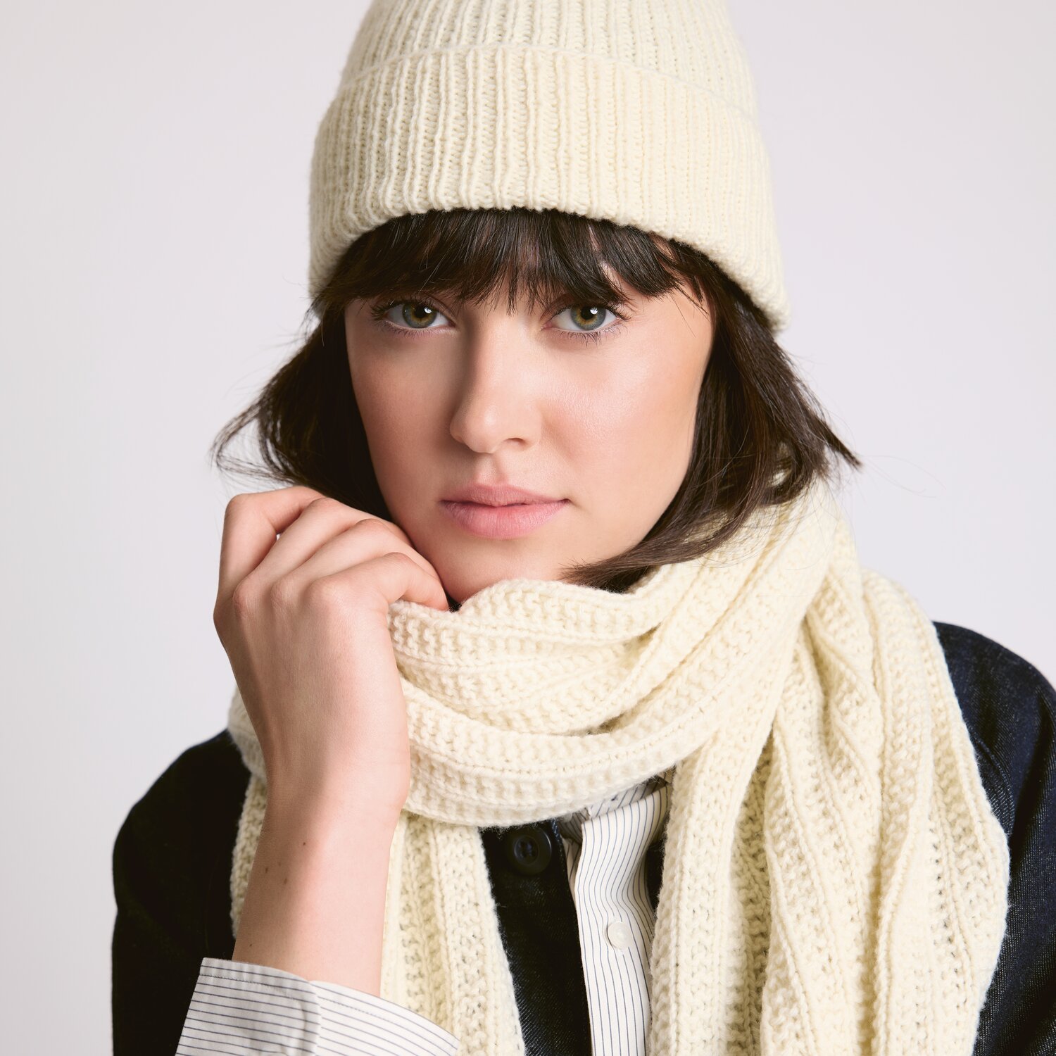 Strickset Schal Modell 07 aus Luxury Knits - Premium Natural Fibres von Rico Design Strickset Mütze Modell 06 aus Luxury Knits - Premium Natural Fibres. Frau trägt cremefarbene Mütze und Schal.
