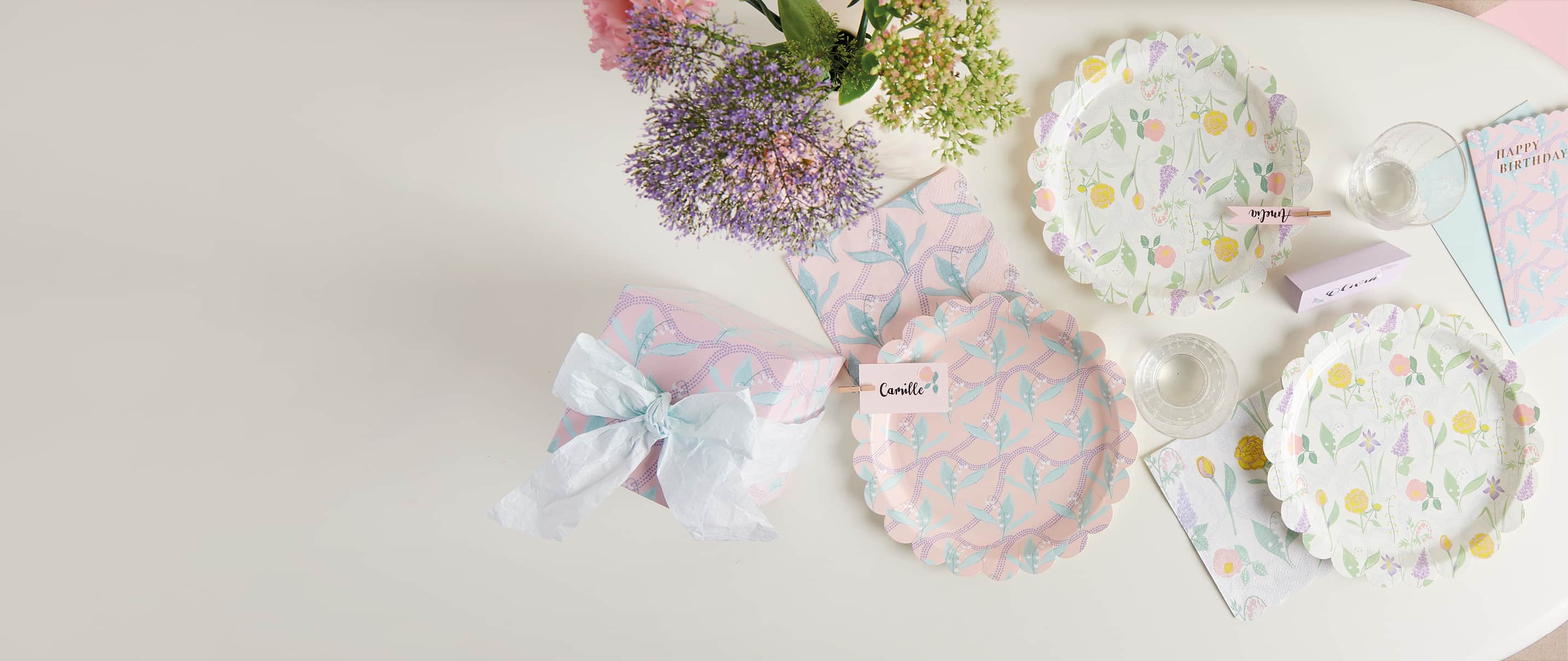 Pappteller und Servietten mit Blumenmustern sind auf einem Tisch dekoriert. 