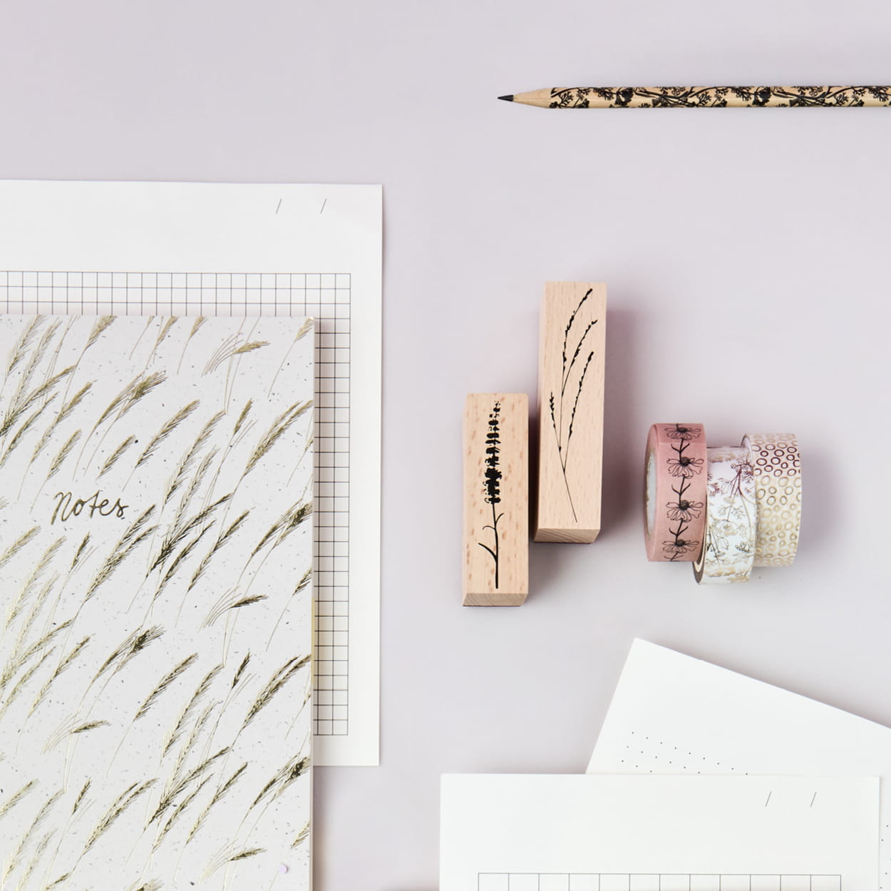 Notizheft, Tapes und Stempel aus der Kollektion In the Meadow liegen auf grauem Hintergrund. 