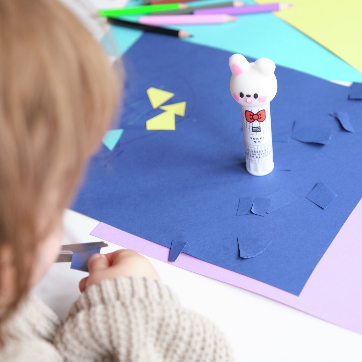 Paper Poetry Klebestift Hase Weiß auf buntem Bastelpapier, Kind schneidet Formen aus.