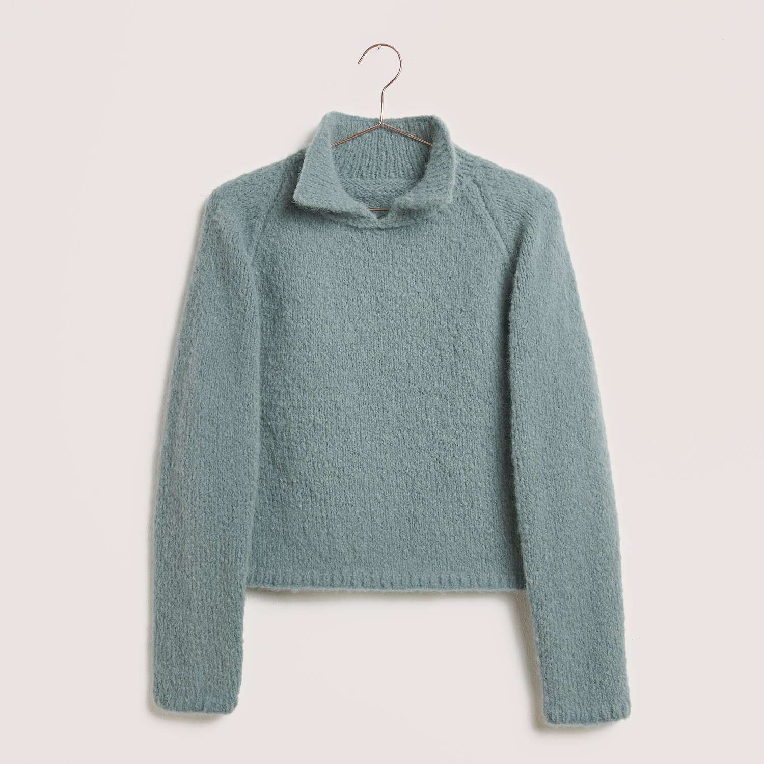 Made by Me No. 21 Herbst-Winter Sprachauswahl deutsch von Rico Design Strickset Pullover Modell 13a aus Made by Me No. 21 in Rauchblau, gefertigt aus Luxury Pure Baby Alpaca, präsentiert auf einem Kleiderbügel.