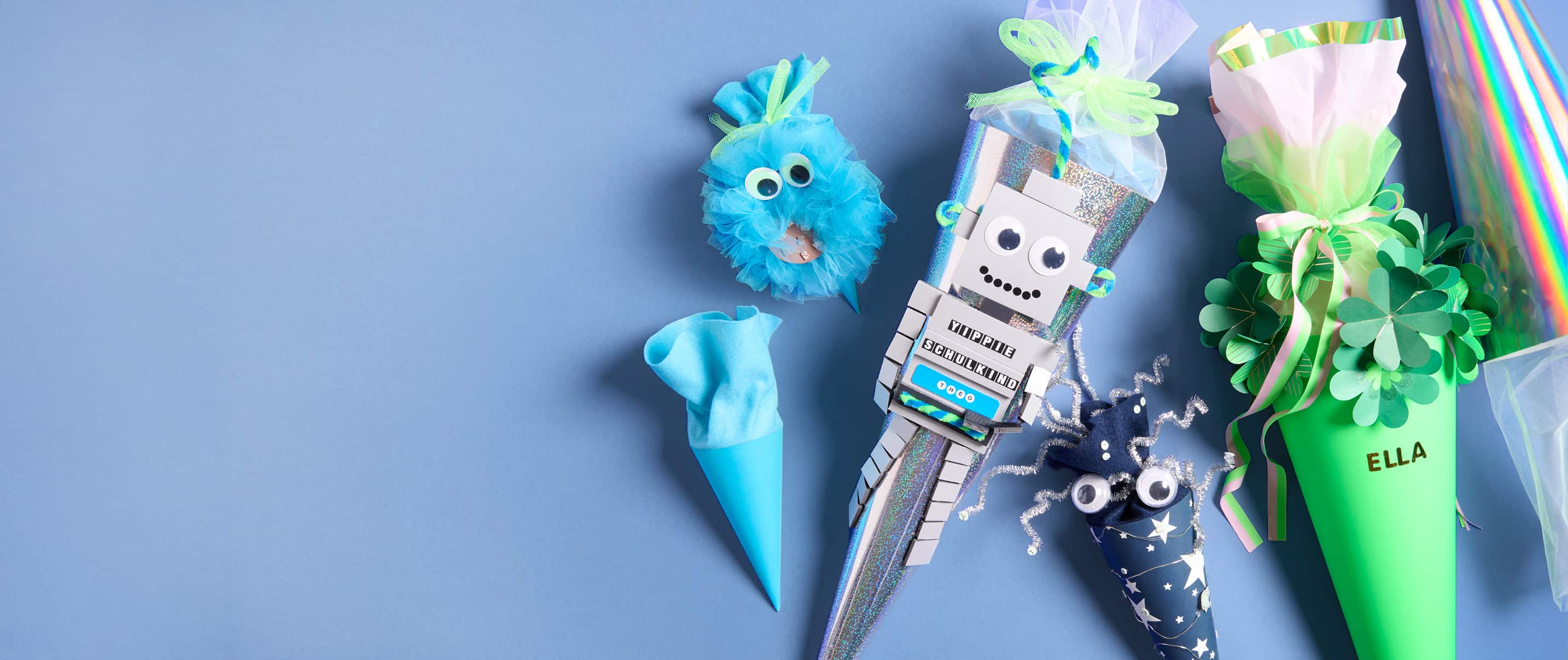 Gebastelte Schultüten in verschiedenen Größen und Designs liegen auf blauem Hintergrund. Eine Schultüte ist mit Roboter-Motiv, eine weitere ist grün mit Kleeblättern 