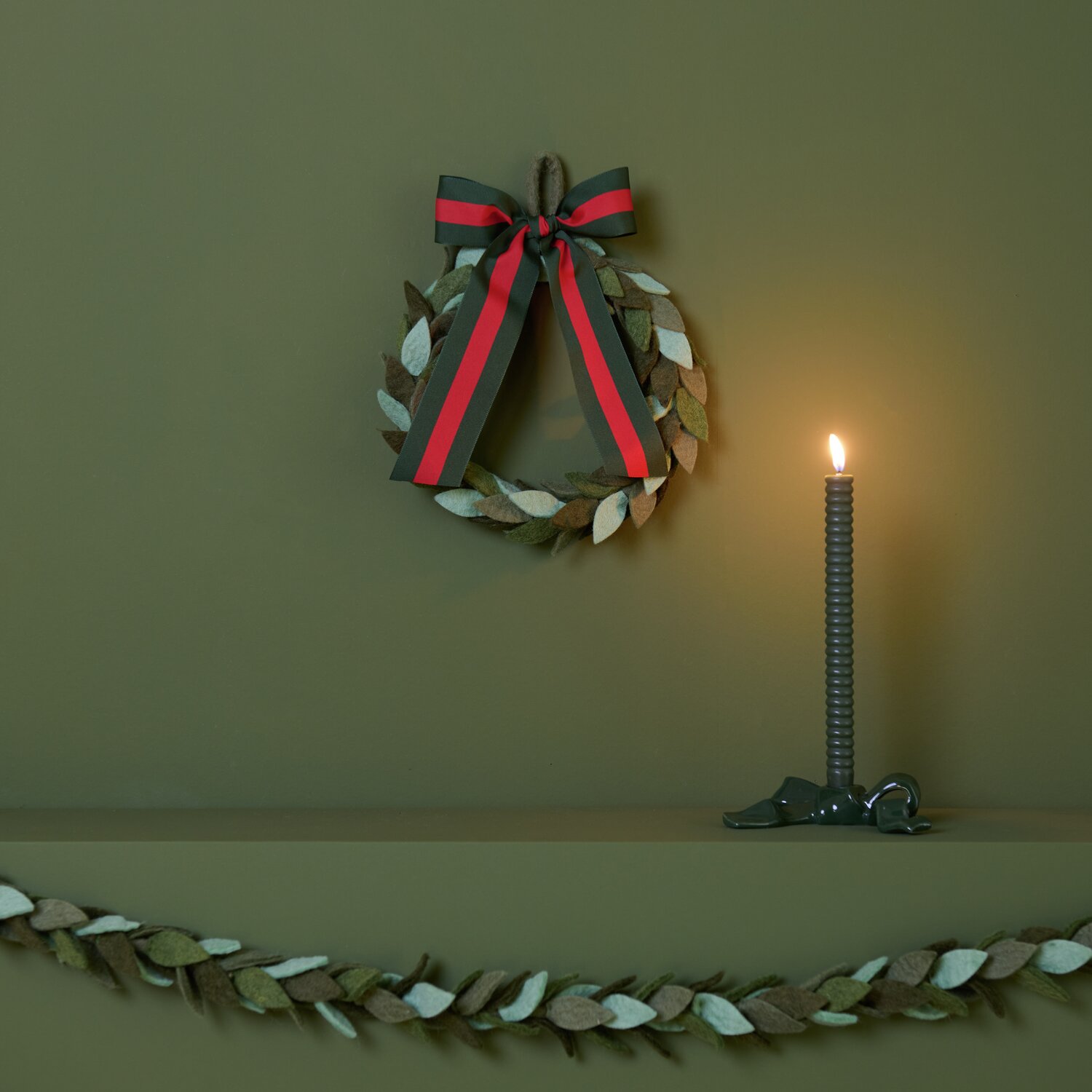 Filz-Blätterkranz Grün mit Keramik Kerzenhalter und Schleife von Rico Design, dekoriert auf einem Regal mit brennender Kerze.