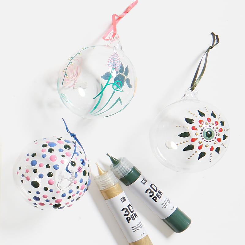 Dekorativ verzierte Glasanhänger mit 3D Effekten liegen mit 3D Pens auf grauem Hintergrund.